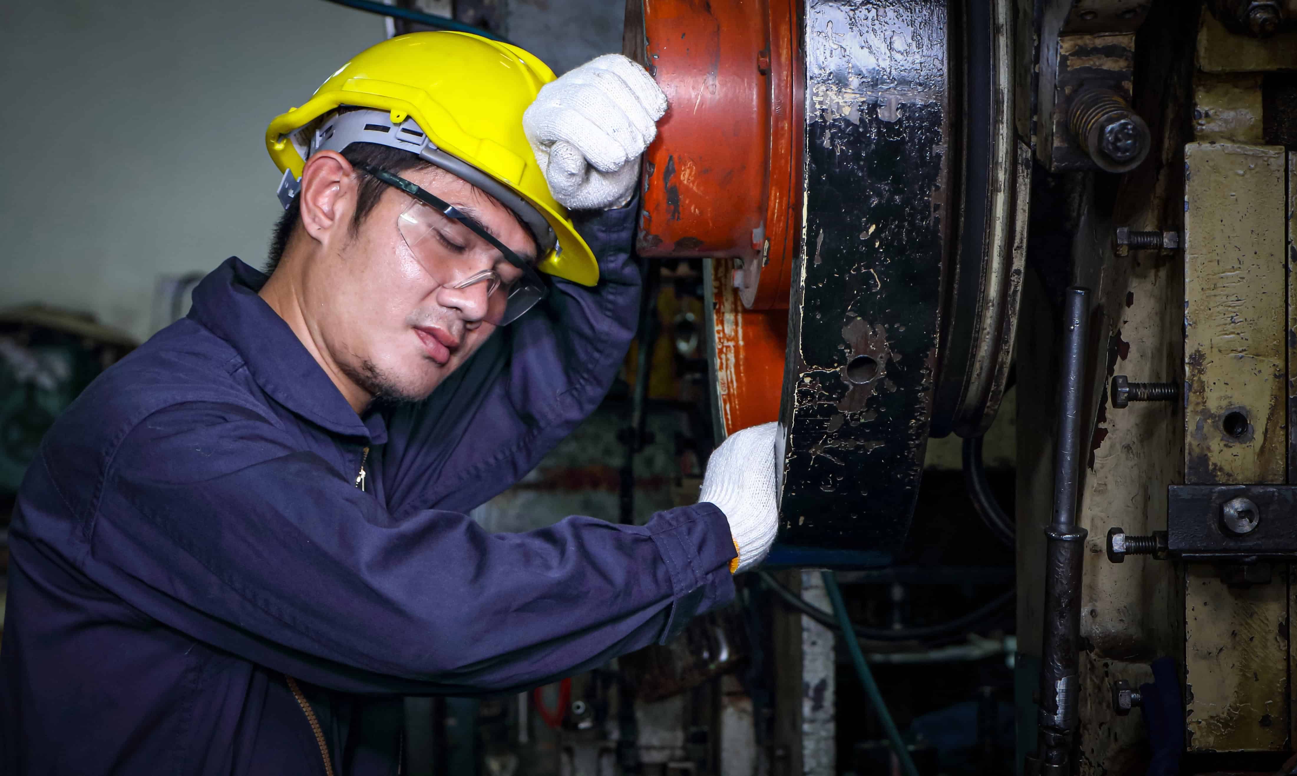 Exhausted industrial worker leaning against machinery, showing the fatigue that builds unseen before an incident.