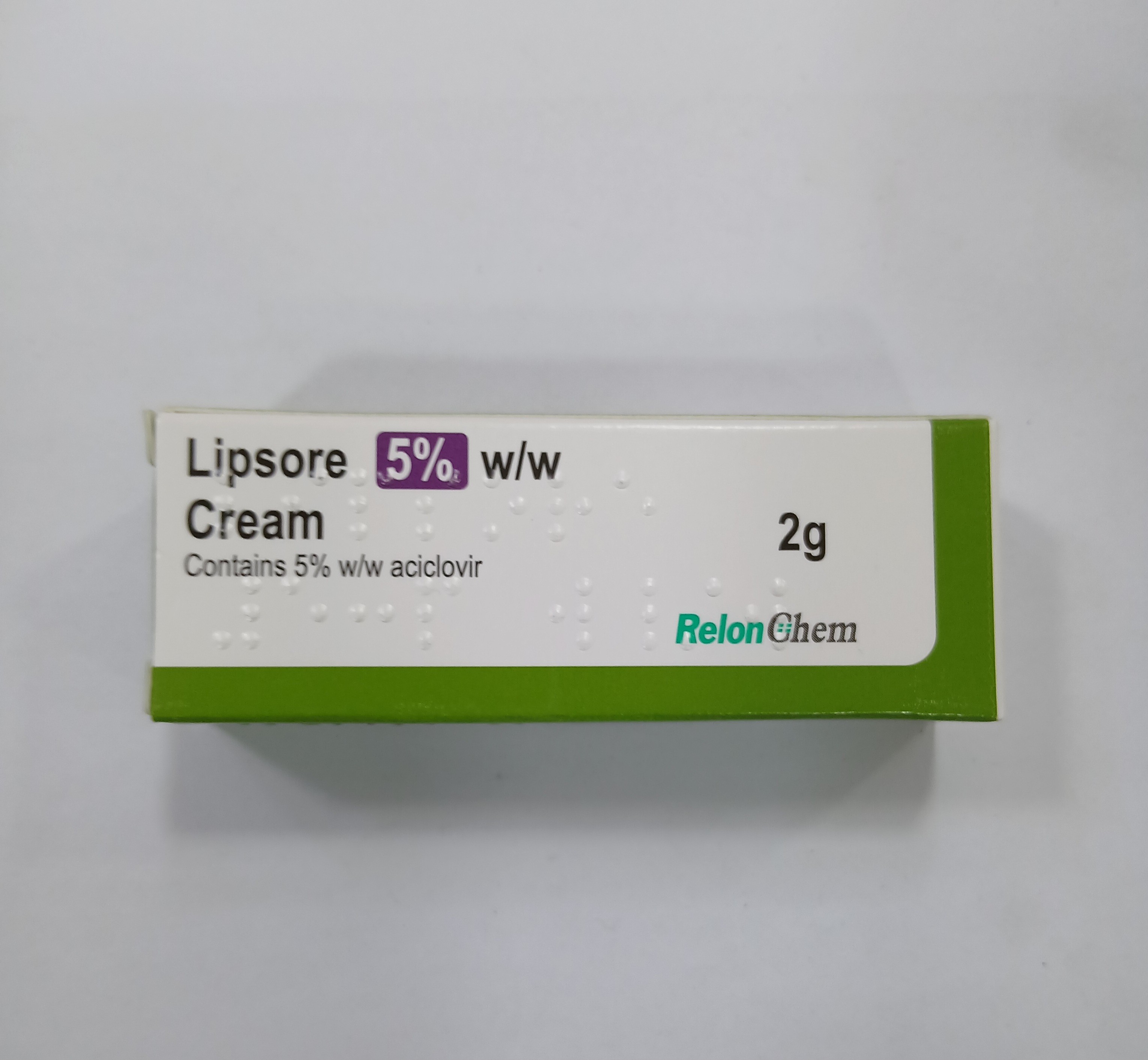 A small white and green cardboard tube packaging displays printed text indicating it contains 2 grams of 5 percent w/w acyclovir cream.