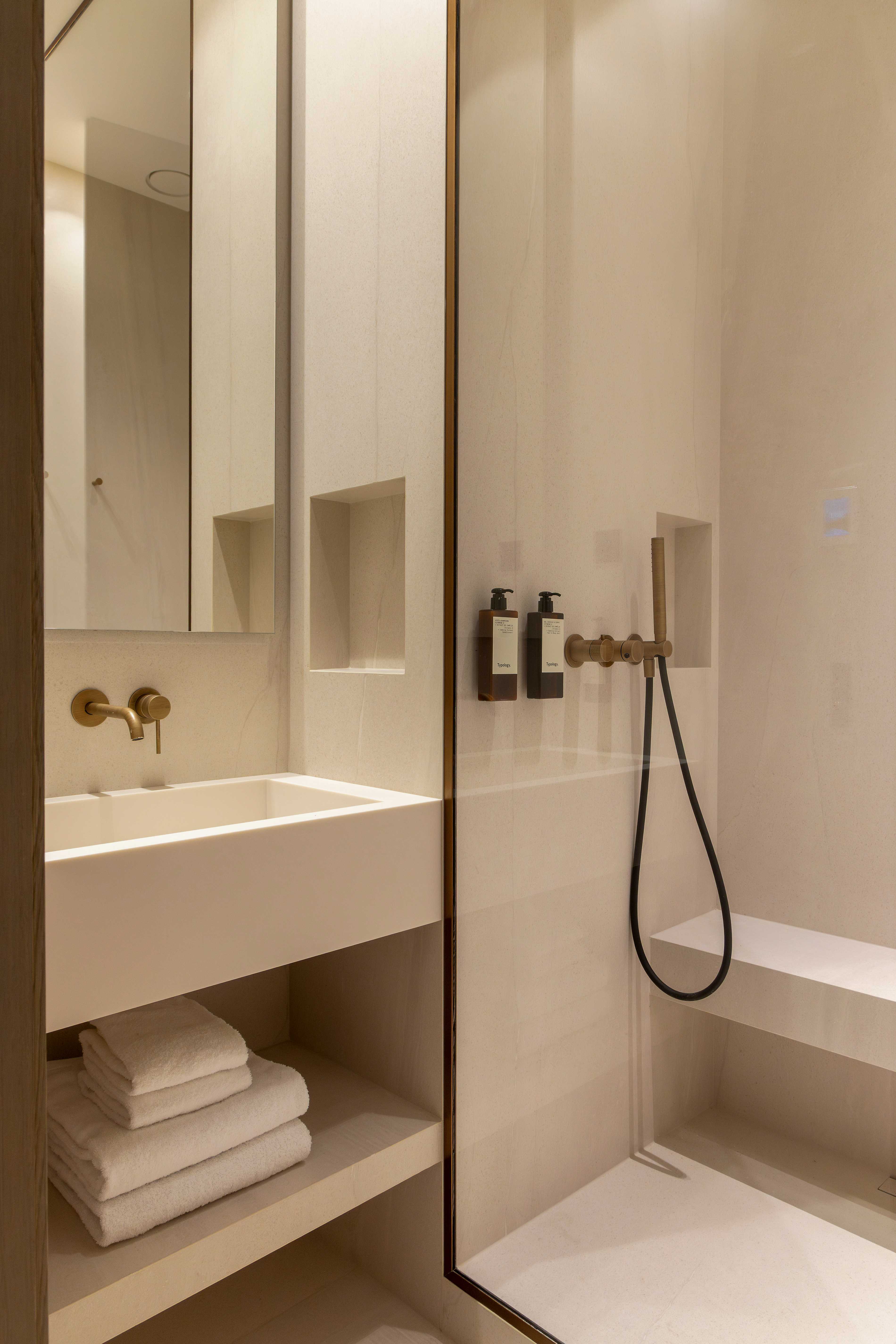 Salle de bains avec vasque blanche, robinetterie doree, miroir, douche italienne et serviettes pliees