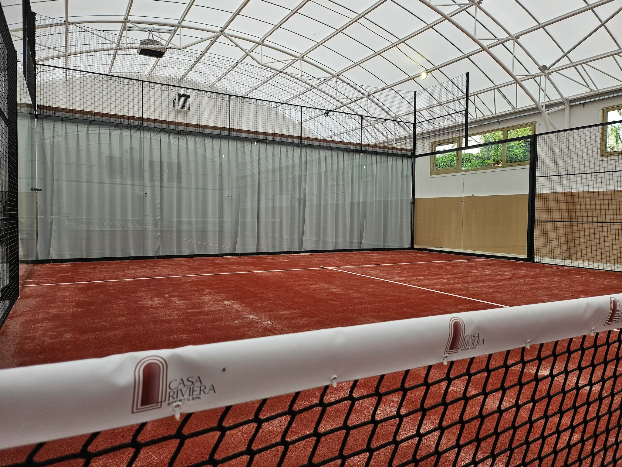 Terrain de Padel intérieur rouge, filet au premier plan. Idéal pour pratiquer le padel.