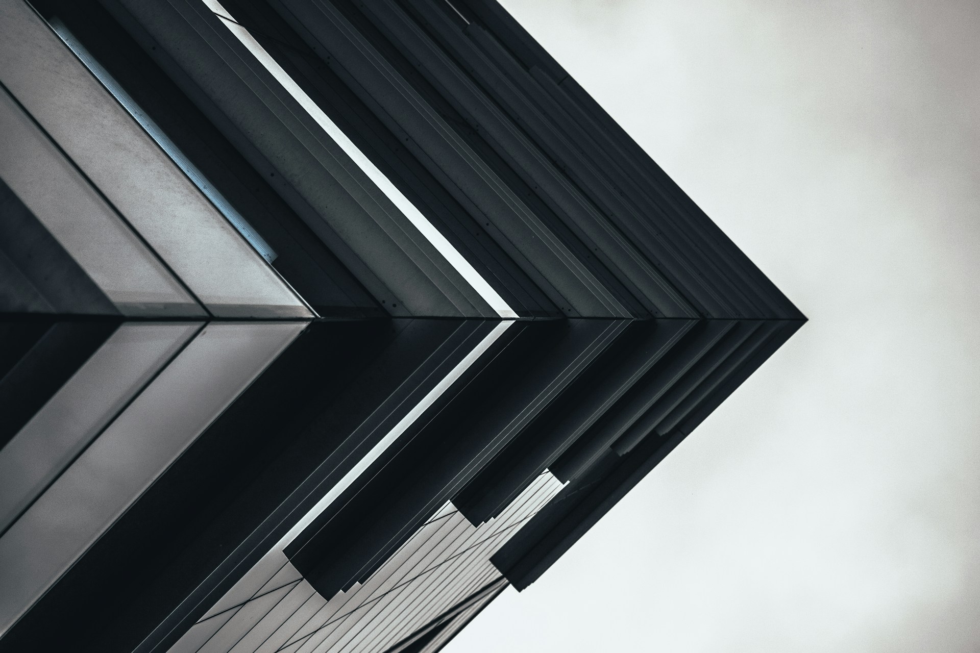 Low-angle photo of a modern building's sharp geometric facade against a pale sky