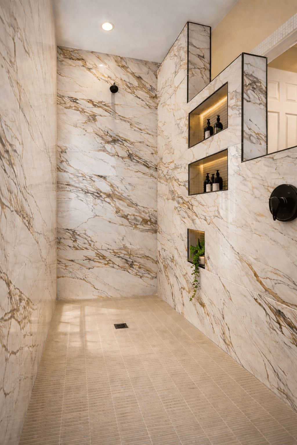 Modern bathroom featuring a walk-in shower, wooden vanity, round mirror, and elegant marble tiles.