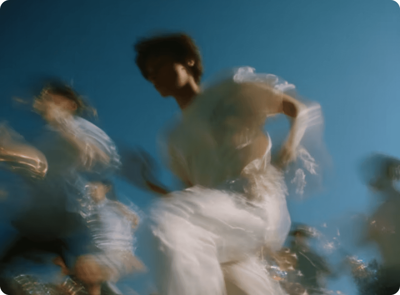 Blurred image capturing the movement of several people dancing energetically under a clear blue sky, creating a dynamic and vibrant atmosphere.