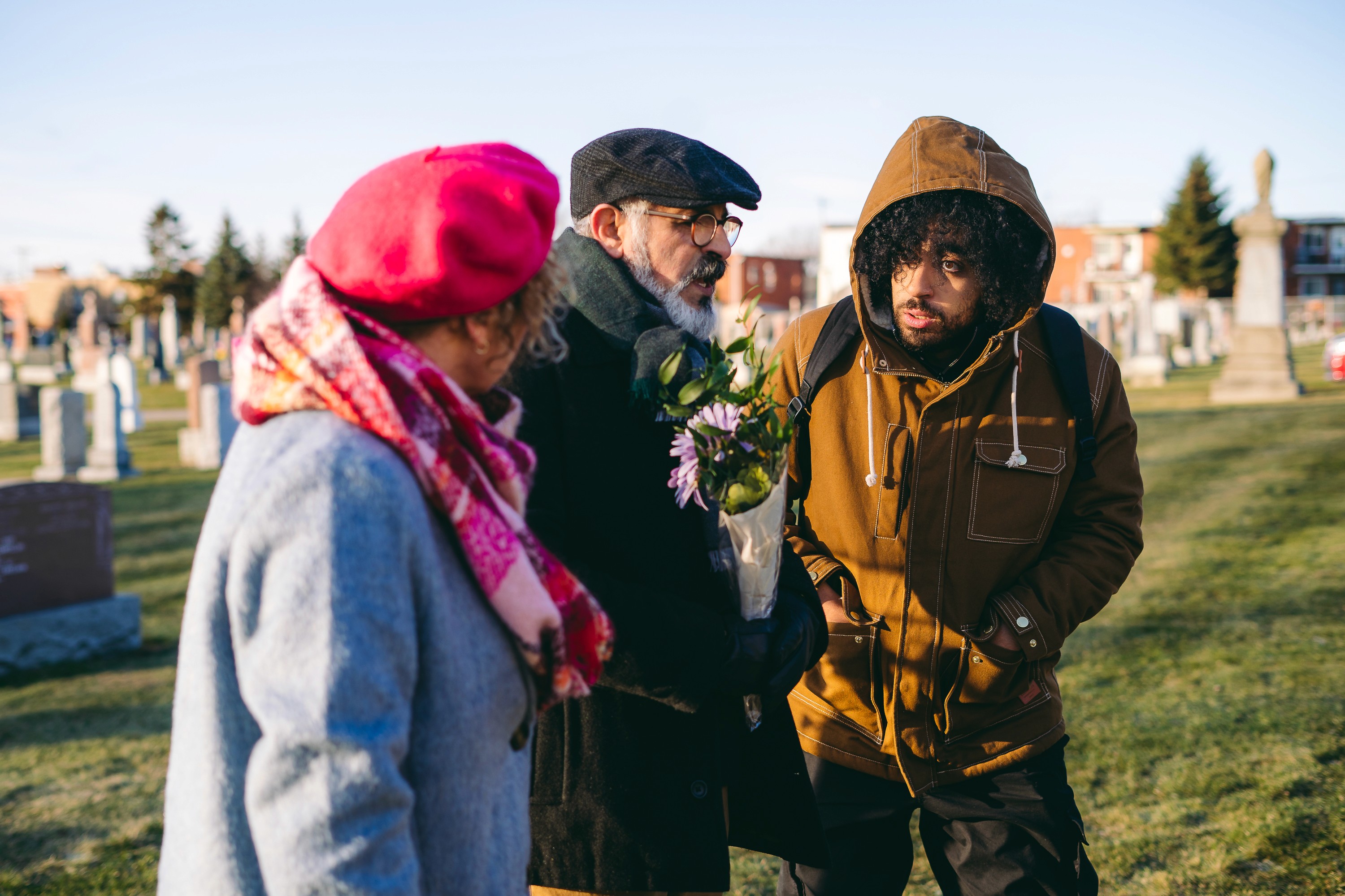 trois personnes dans un cimetière, l'une d'entre elle tient un bouquet de fleurs.