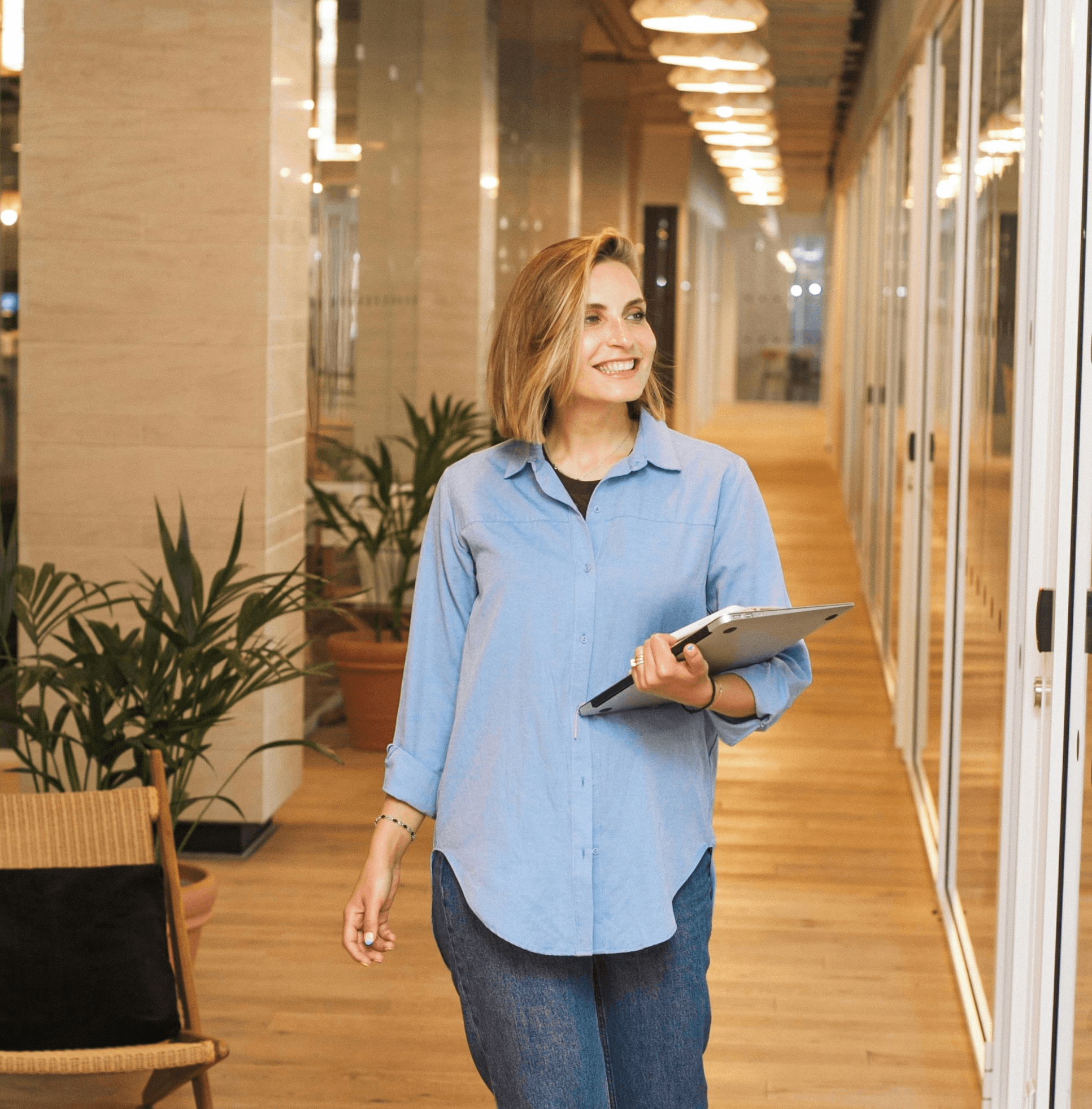 woman in blue dress shirt and blue denim jeans standing beside brown wooden chair