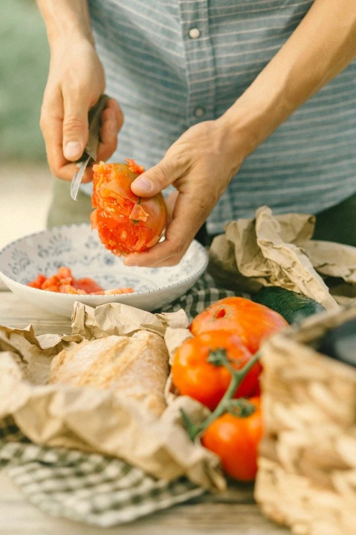 Hands peeling ripe tomatoes at an outdoor table.