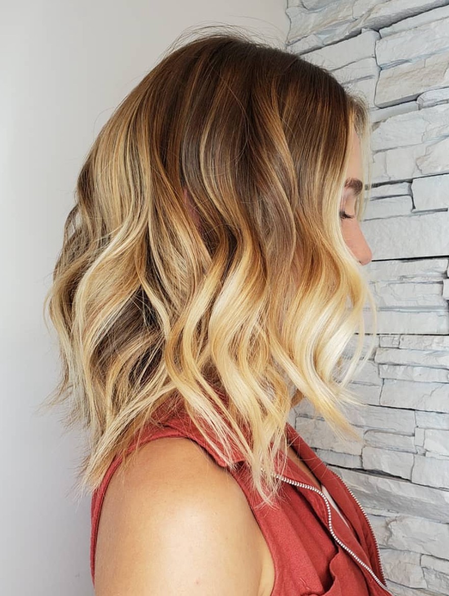 Side view of a textured blonde lob with soft brunette roots and bright balayage, styled in tousled beachy waves for a sunkissed finish.