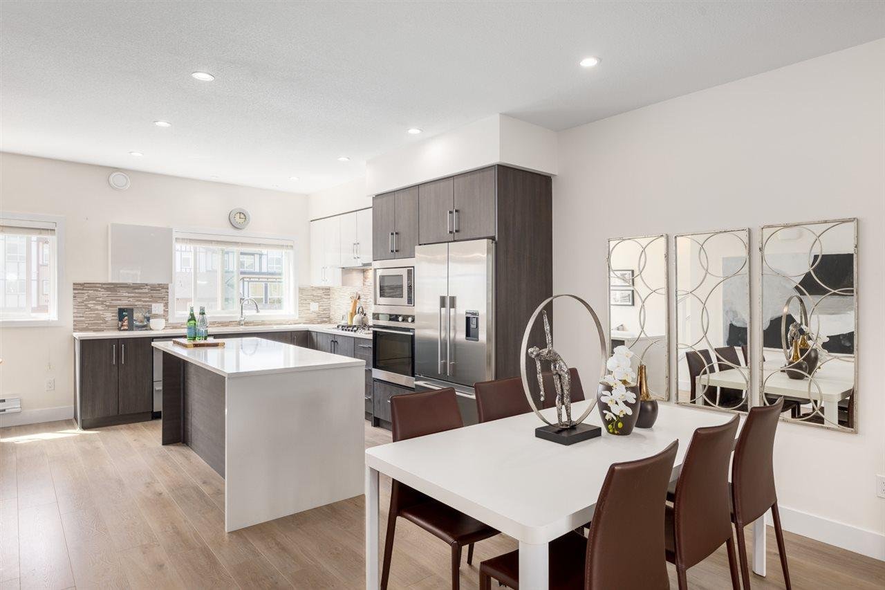 Modern kitchen with dark cabinets and a white countertop, featuring a dining table surrounded by chairs.