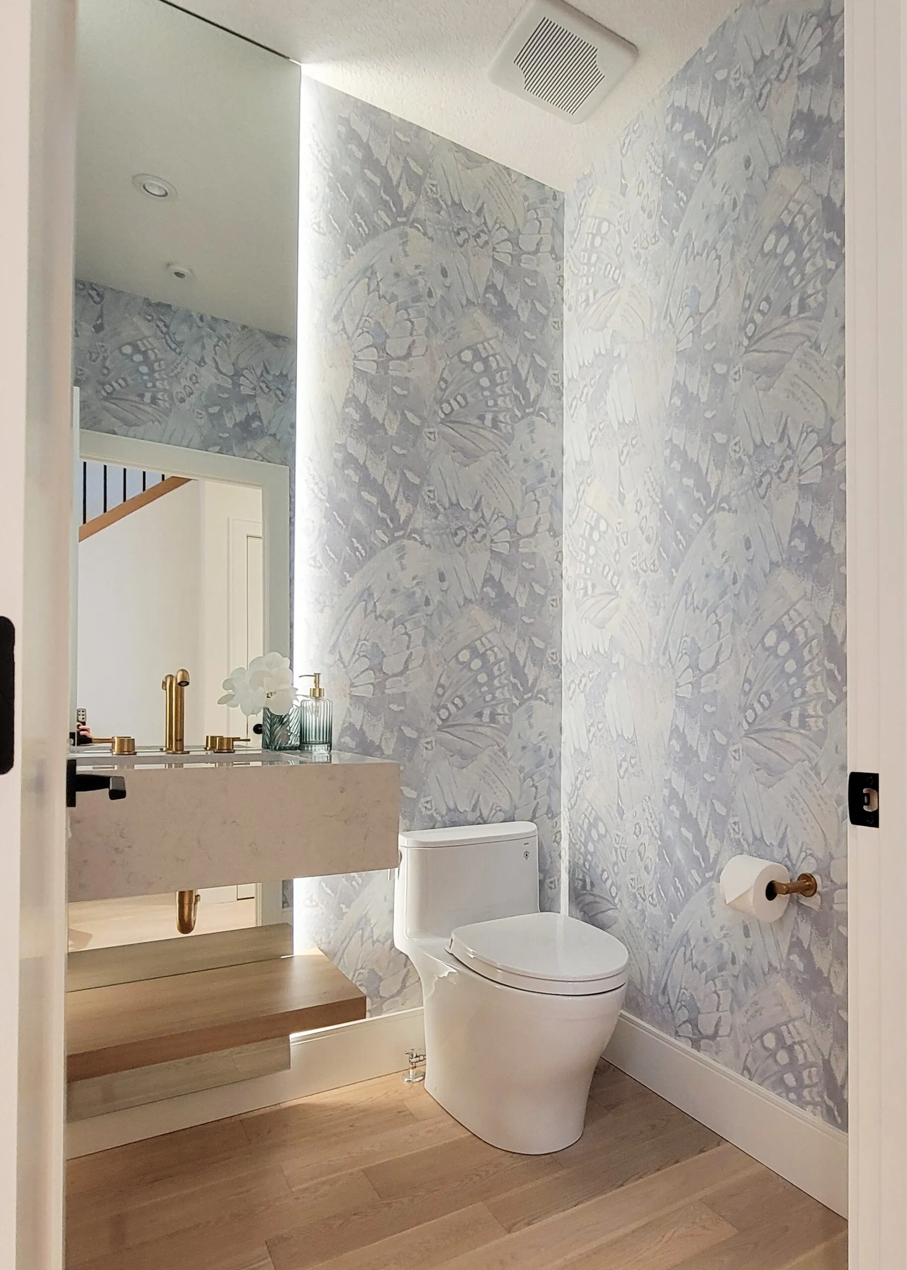 Image of modern powder room with floating vanity, floor to ceiling mirror behind the vanity and blue butterfly wallpaper.