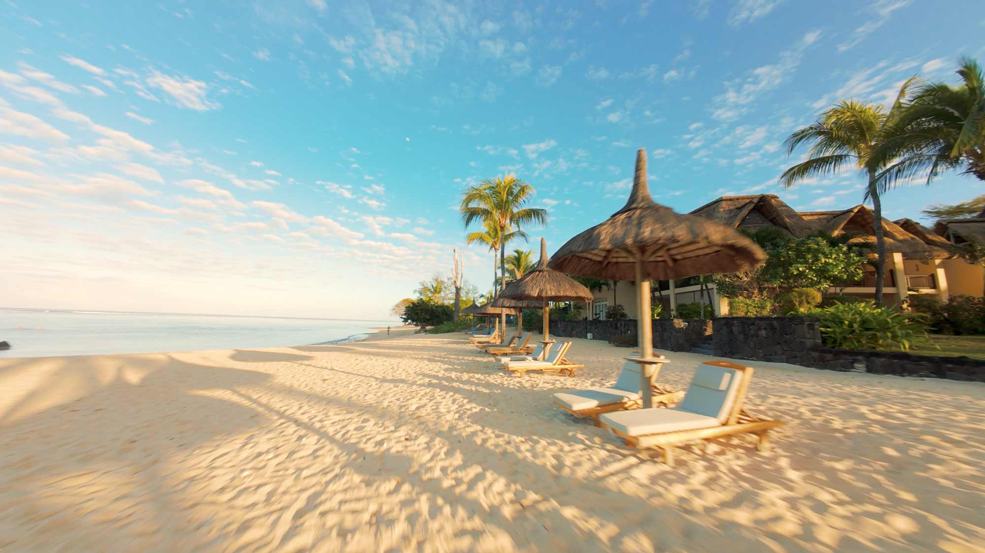 Sunny beach with loungers under palm-thatched shades, filmproduction ad for a hotel in mauritius