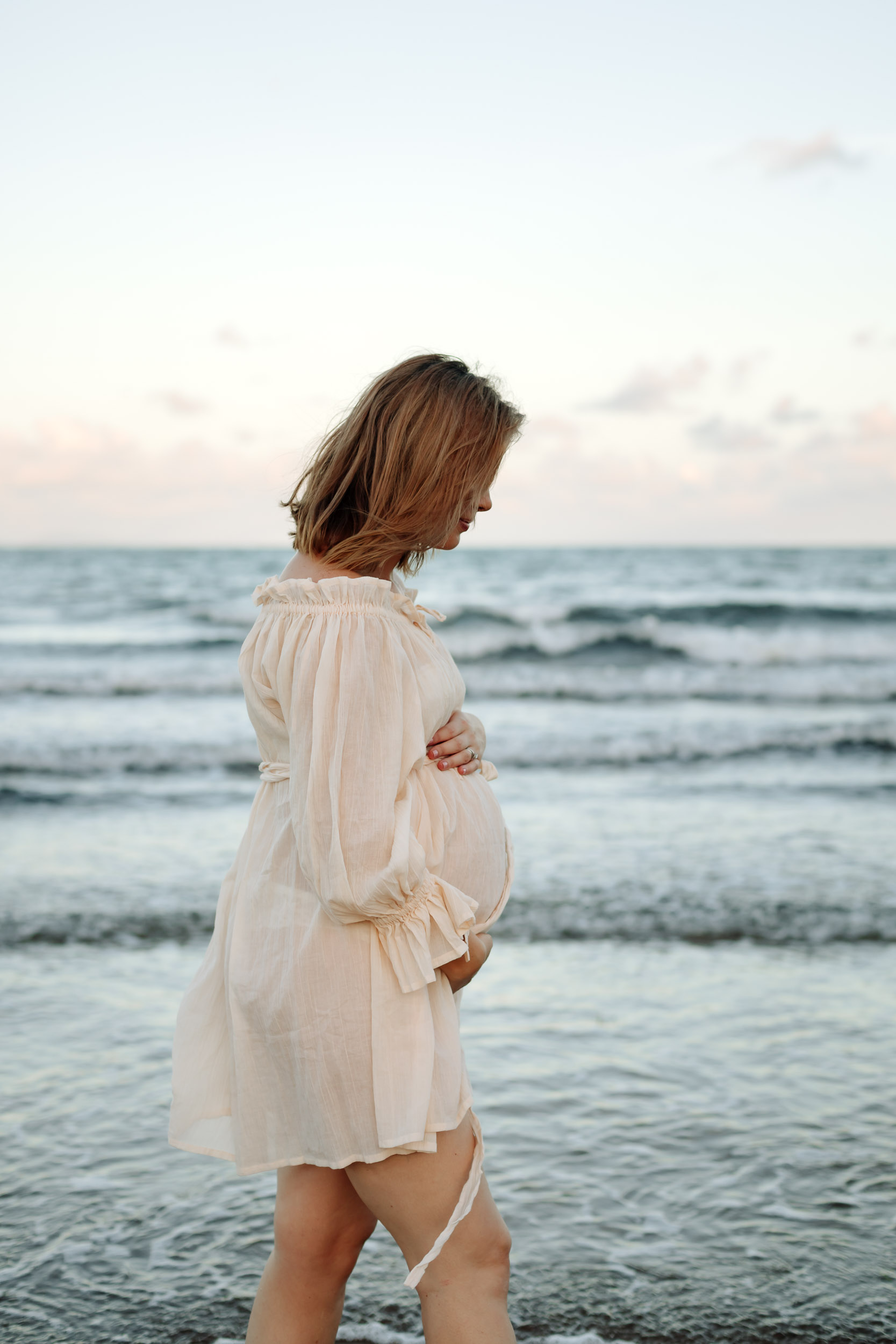 Pregnant mother walking along the shoreline during a Mackay maternity photography session at sunset with warm coastal light.