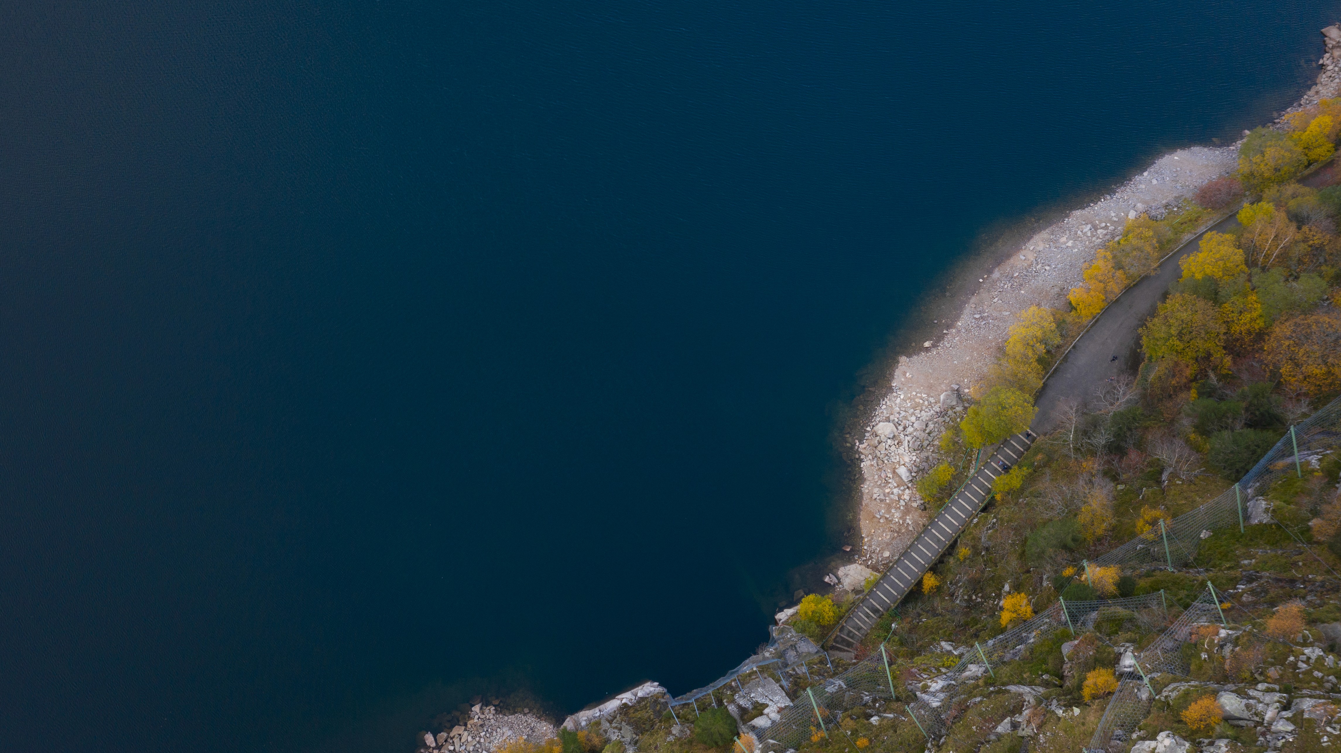 Silhouette of a person with a camera walking towards vibrant orange light under dim blue streetlights on a misty road at night. Mysterious and atmospheric.