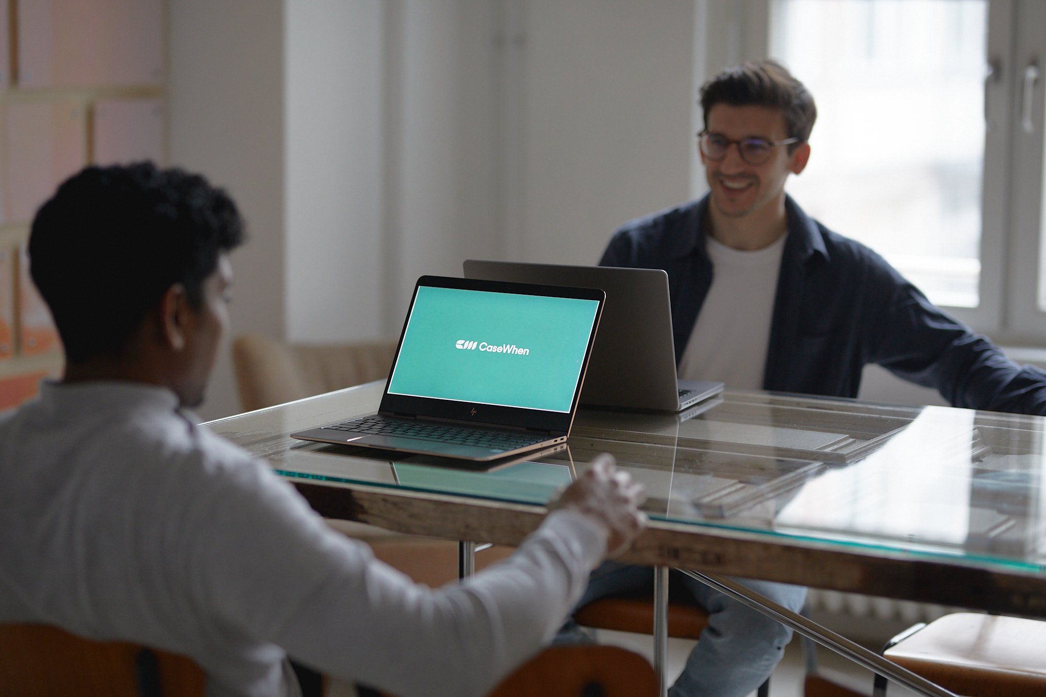 CaseWhen Consulting founders, Sajagan Thirugnanam and Austin Levine, discussing Power BI solutions in a modern office, with their logo displayed on a laptop screen.