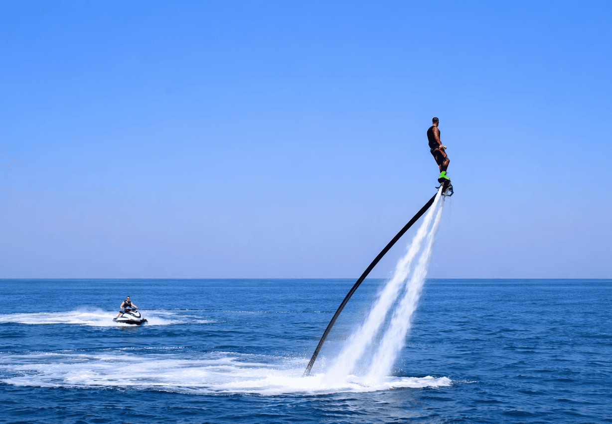 Propelled by water jets, a person hovers high above the water, while a jet ski cruises in the background.