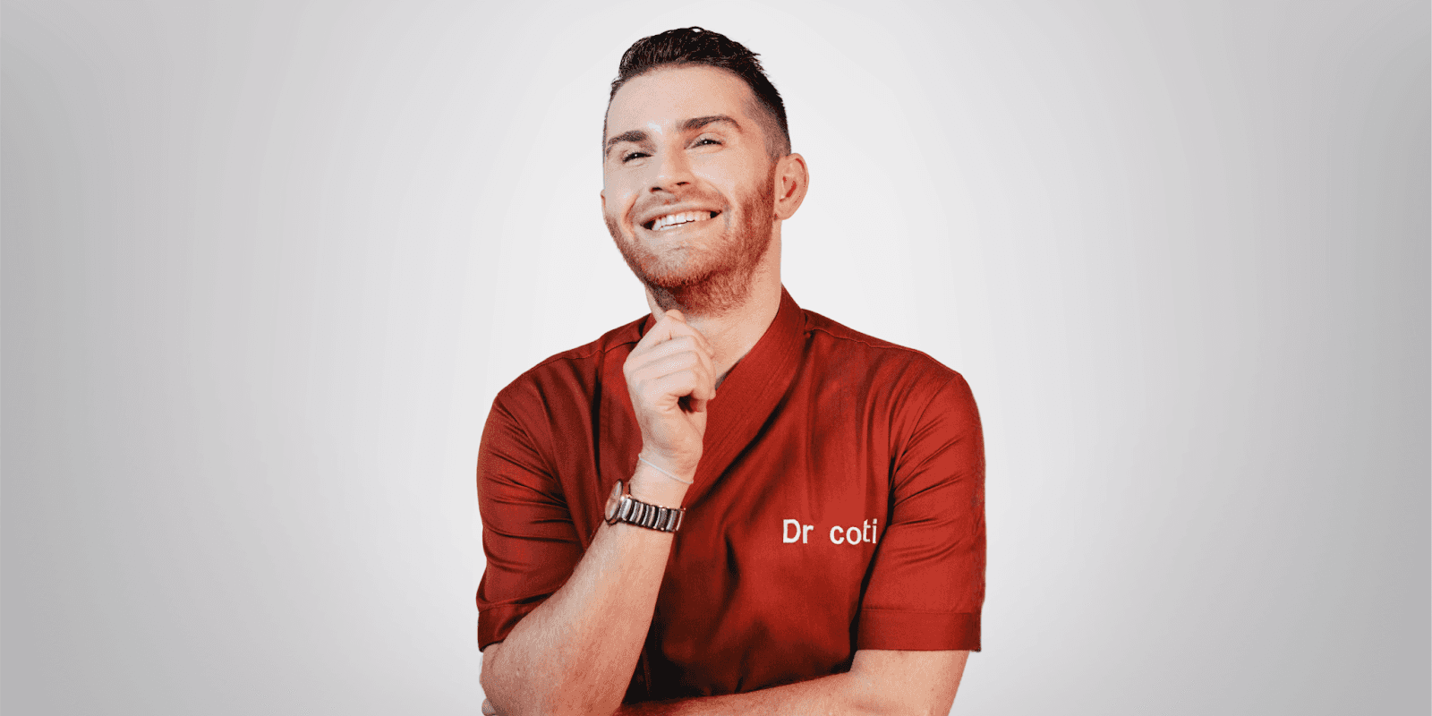 Smiling man in red uniform labeled "Dr. Costi," posing confidently against a plain light background.