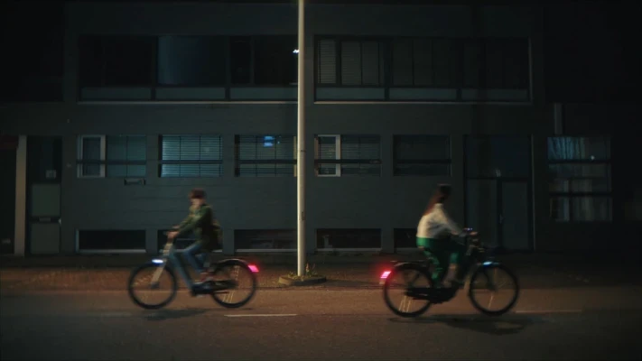 2 people cycling across each other at night