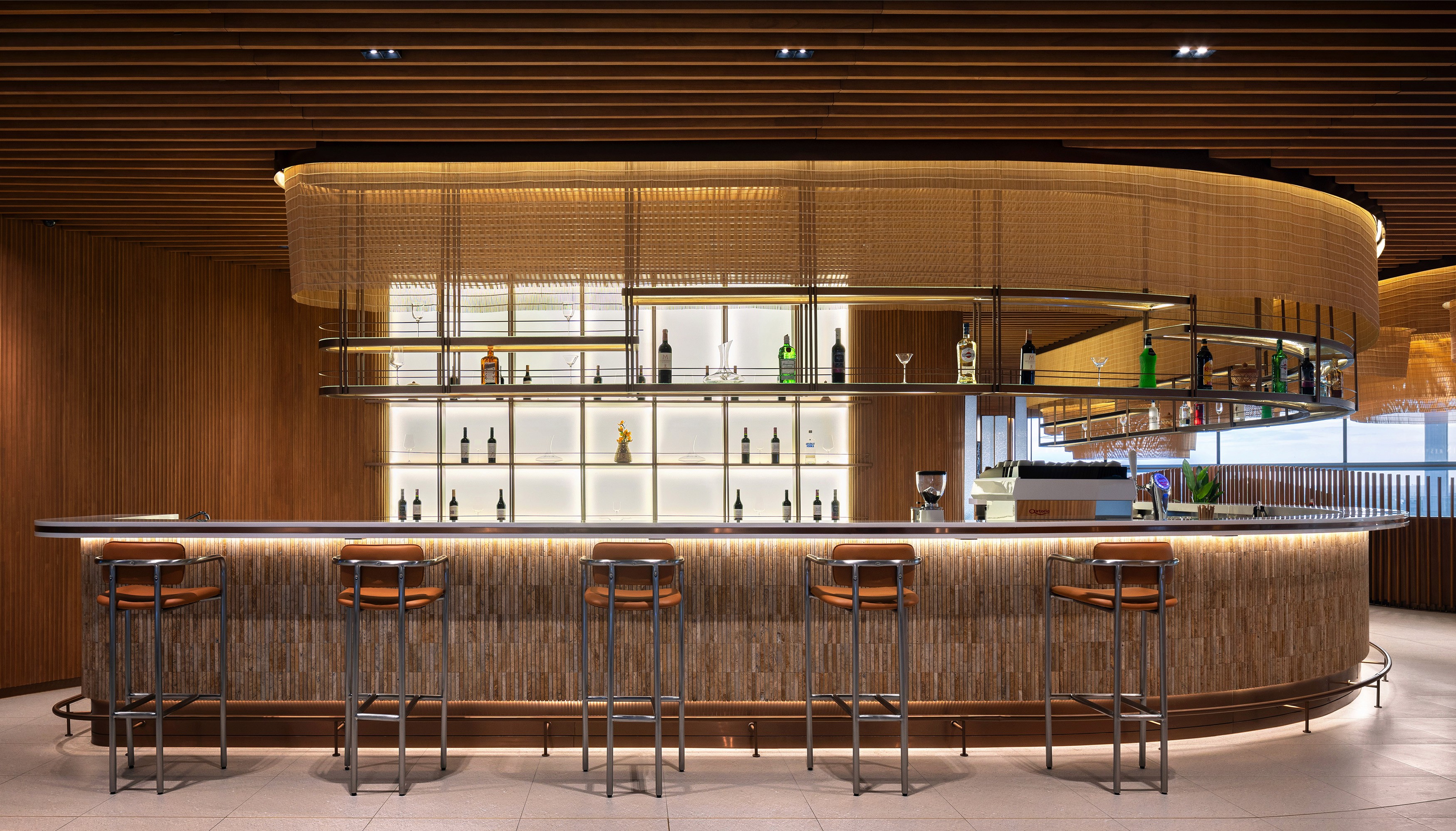 Architectural shot of the circular bar counter with backlit tiered bottle displays and timber finishes highlighting the intersection of operational efficiency and superior interior finishing