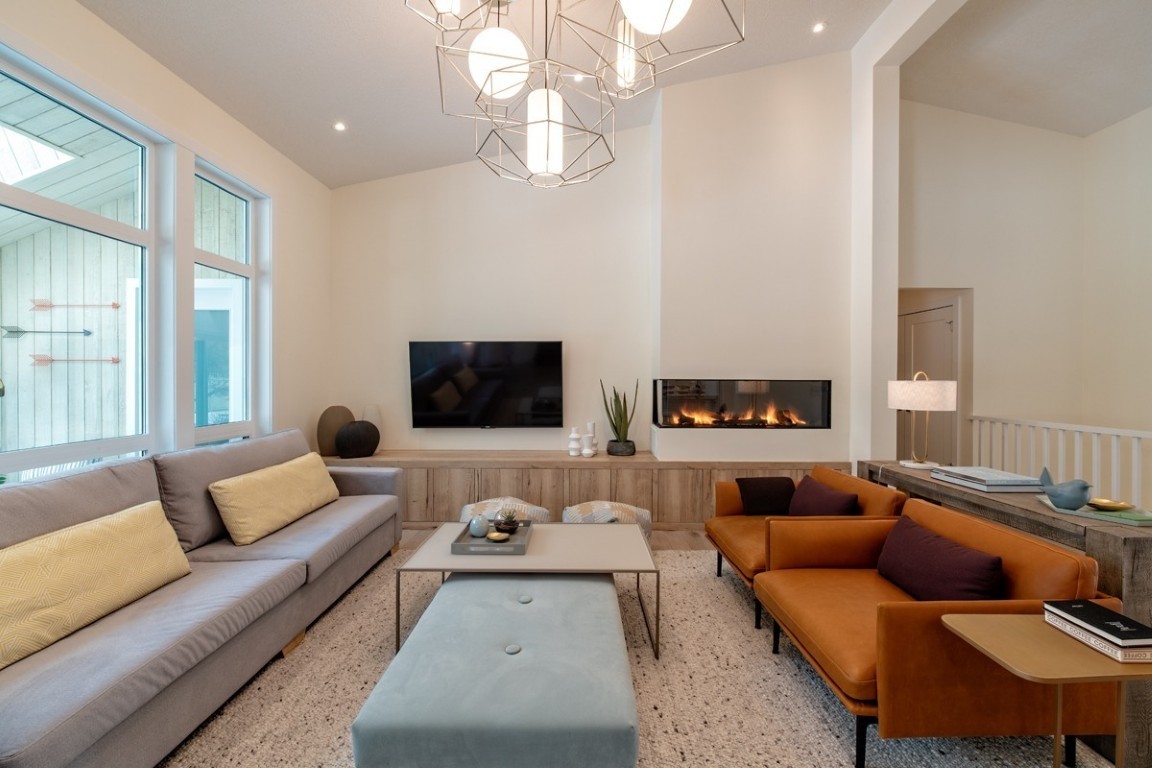 Cozy modern living room with light blue grey couch, two burnt orange large chairs, large windows, and warm fireplace.