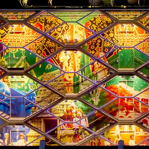 A building's exterior covered in vibrant depictions of cultural and historical elements, framed by a geometric lattice structure.