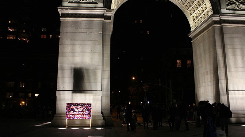 An illuminated and colorful street poster with text on it near a stone arch.