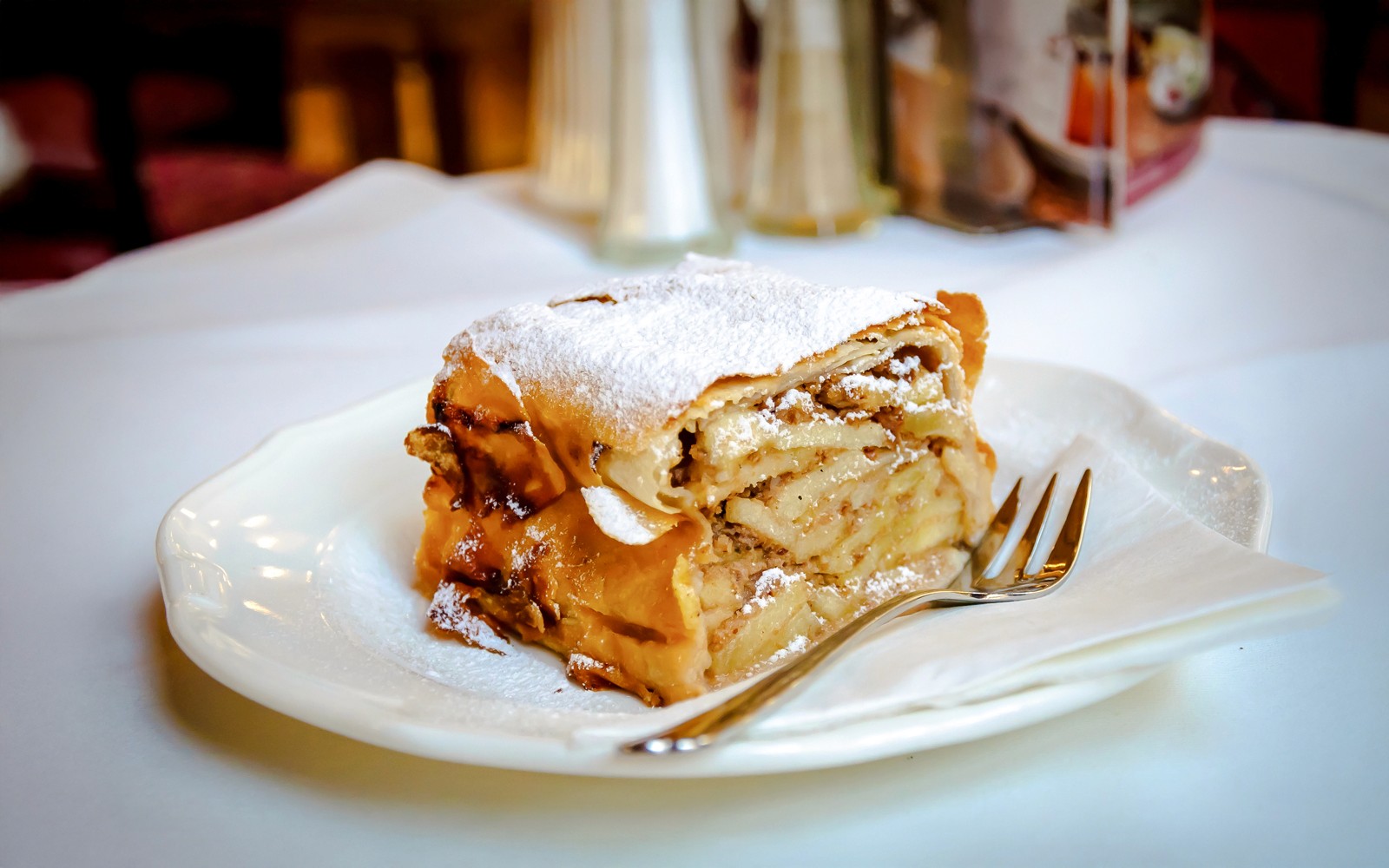Slice of apple strudel with layers of apples and spices on a plate.