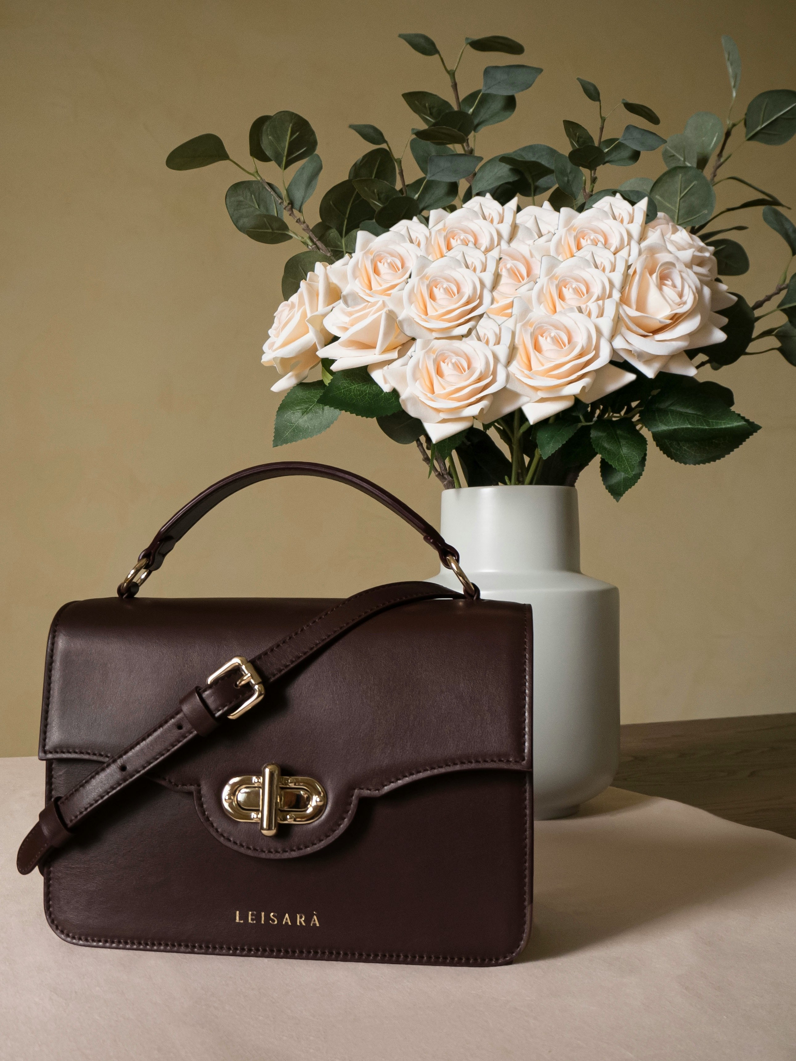 brown leather handbag beside white flower vase