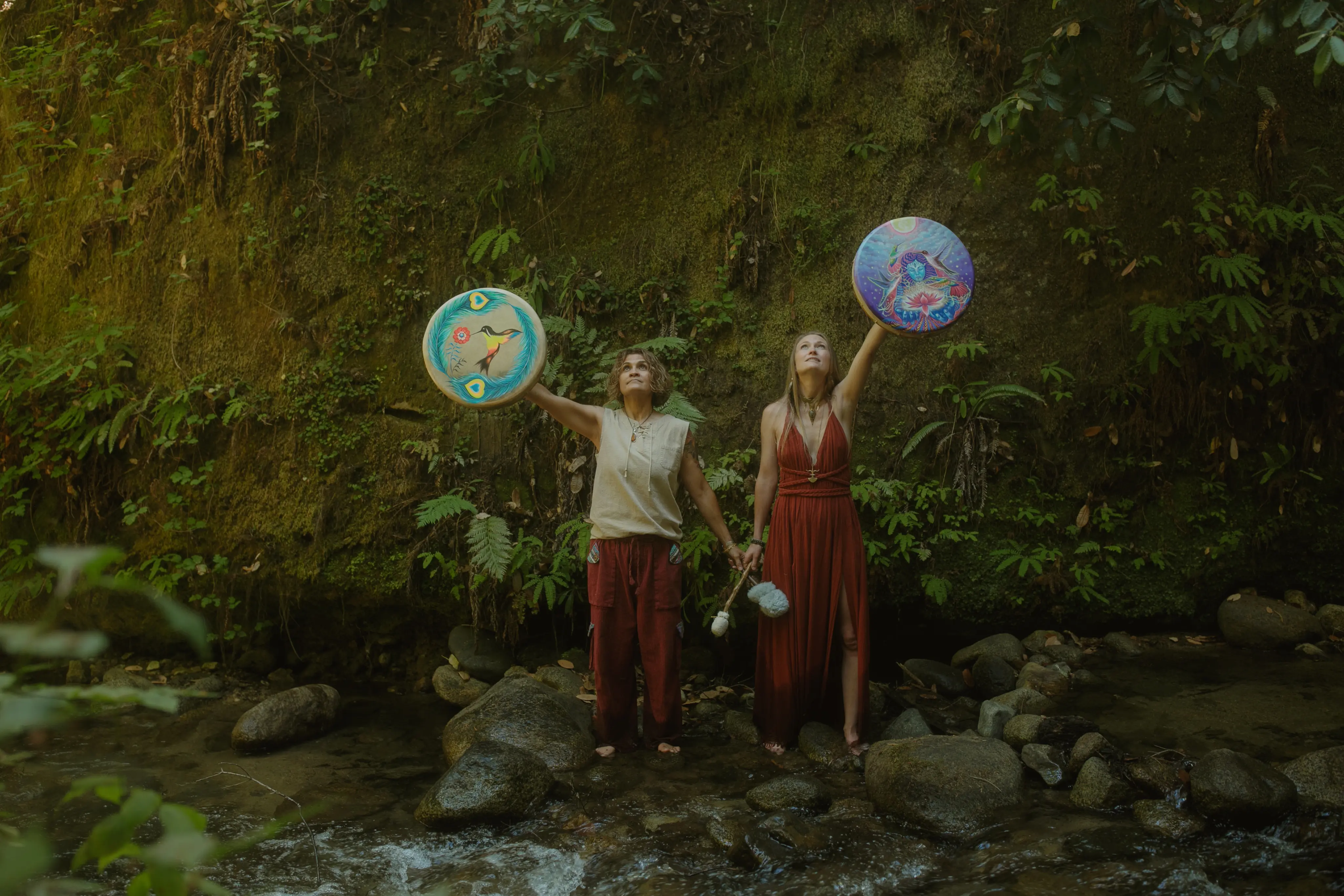 Emeline and Sonia holding sacred ceremonial drums in a jungle stream