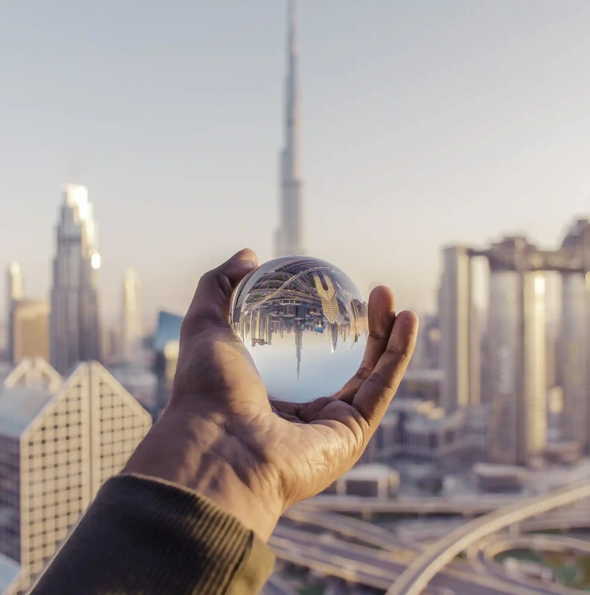 A person holding a glass sphere reflecting a cityscape.