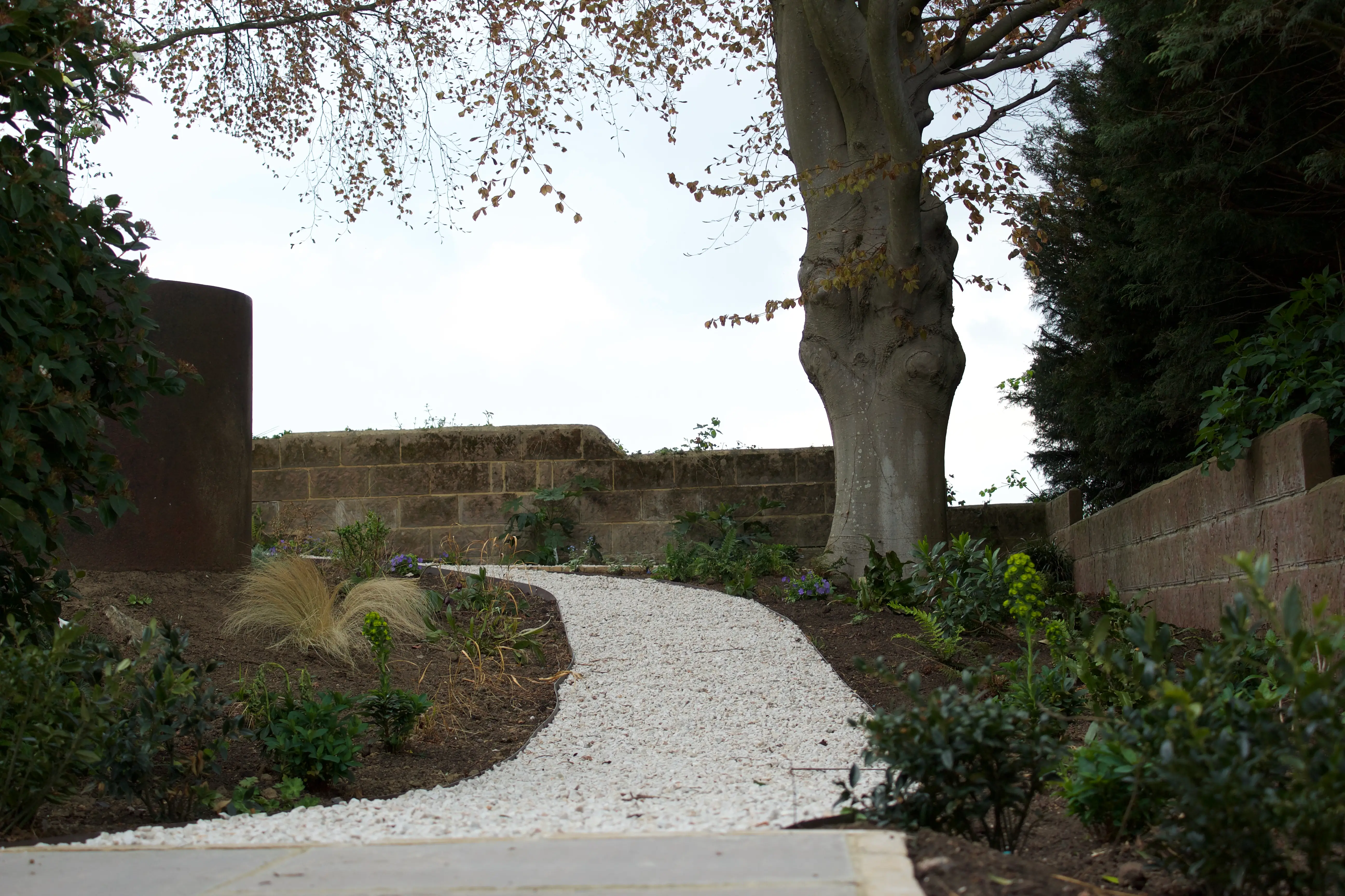 A winding path surrounded by greenery leads towards a distant horizon under a cloudy sky.
