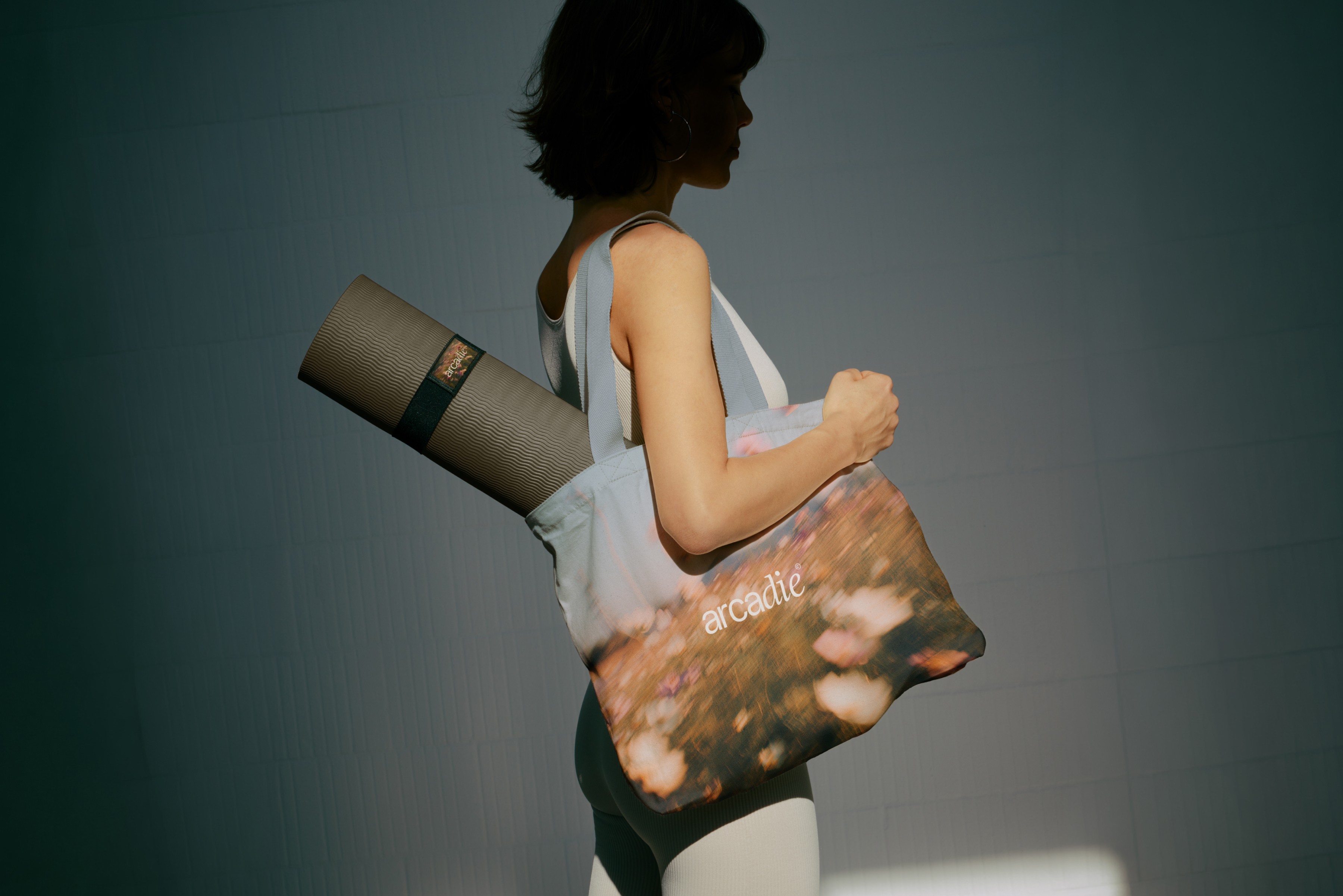 Femme portant un tote bag imprimé de fleurs arcadie et tapis de yoga, image lifestyle douce pour marque de yoga et méditation.