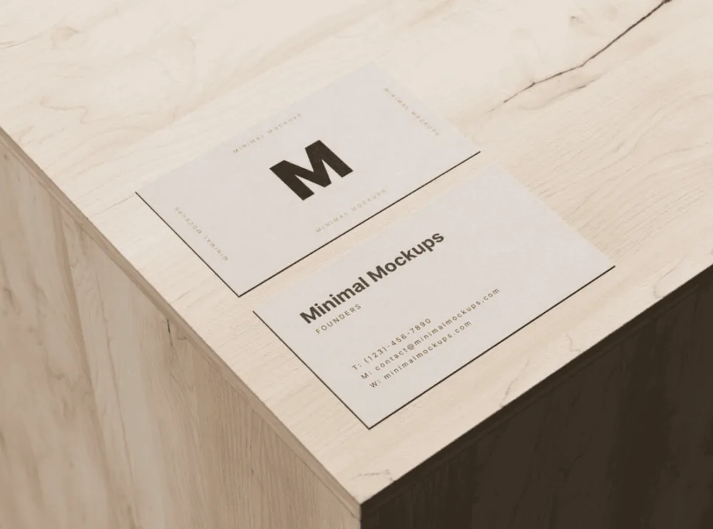 Mockup of two beige business cards on a light wood surface. One card displays a bold logo, while the other showcases text layout with placeholder details, emphasizing a clean and minimal design.
