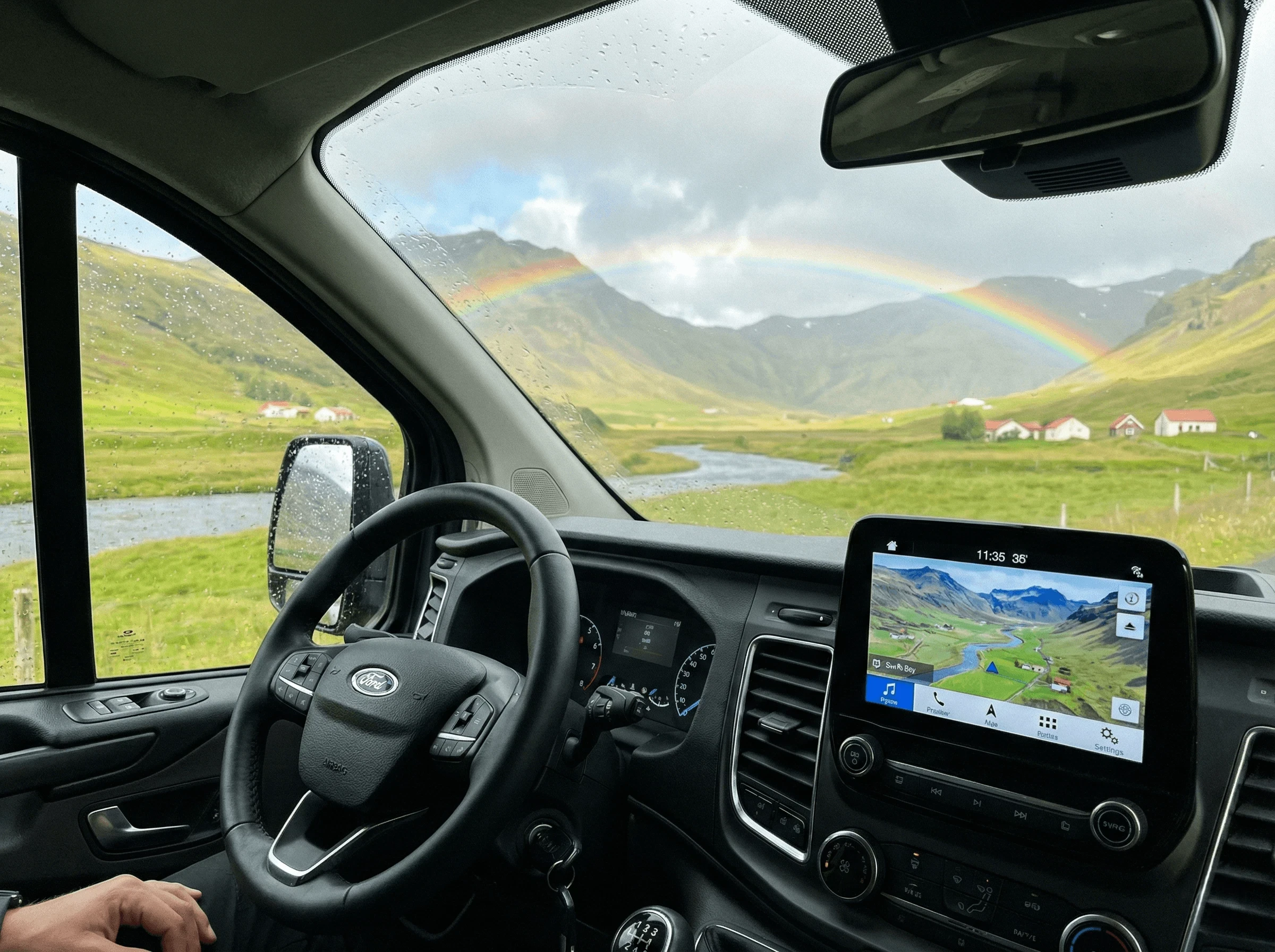 View from the driver's seat looking through the windshield at a lush green valley with a rainbow.