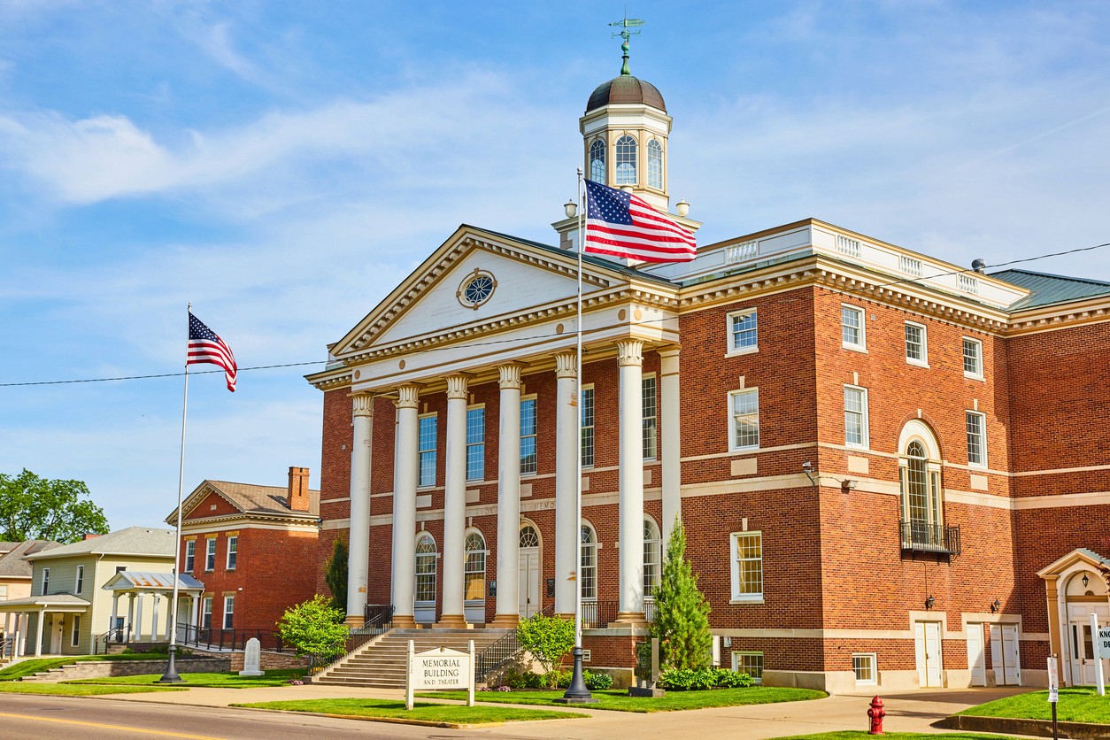A brick memorial building with white pillars and American flags.