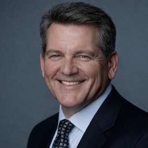 a man with his arms crossed standing in front of a desk