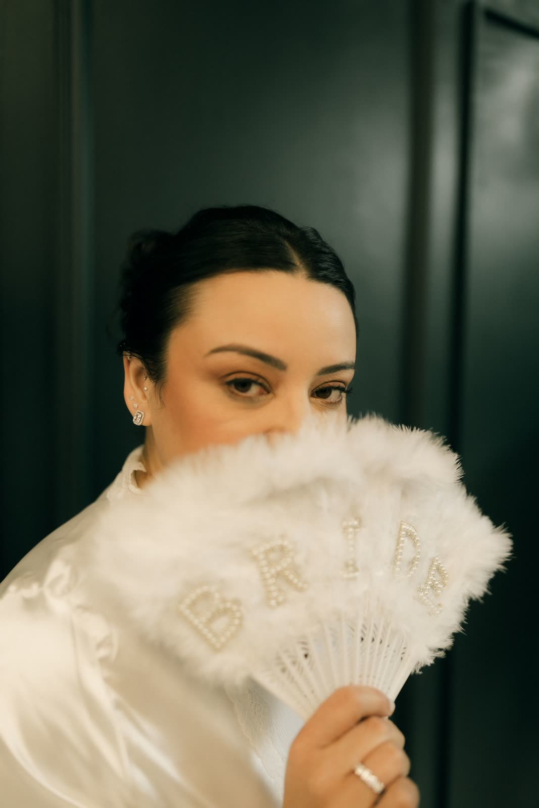 Bride half hidden behind a white feather fan with pearl lettering
