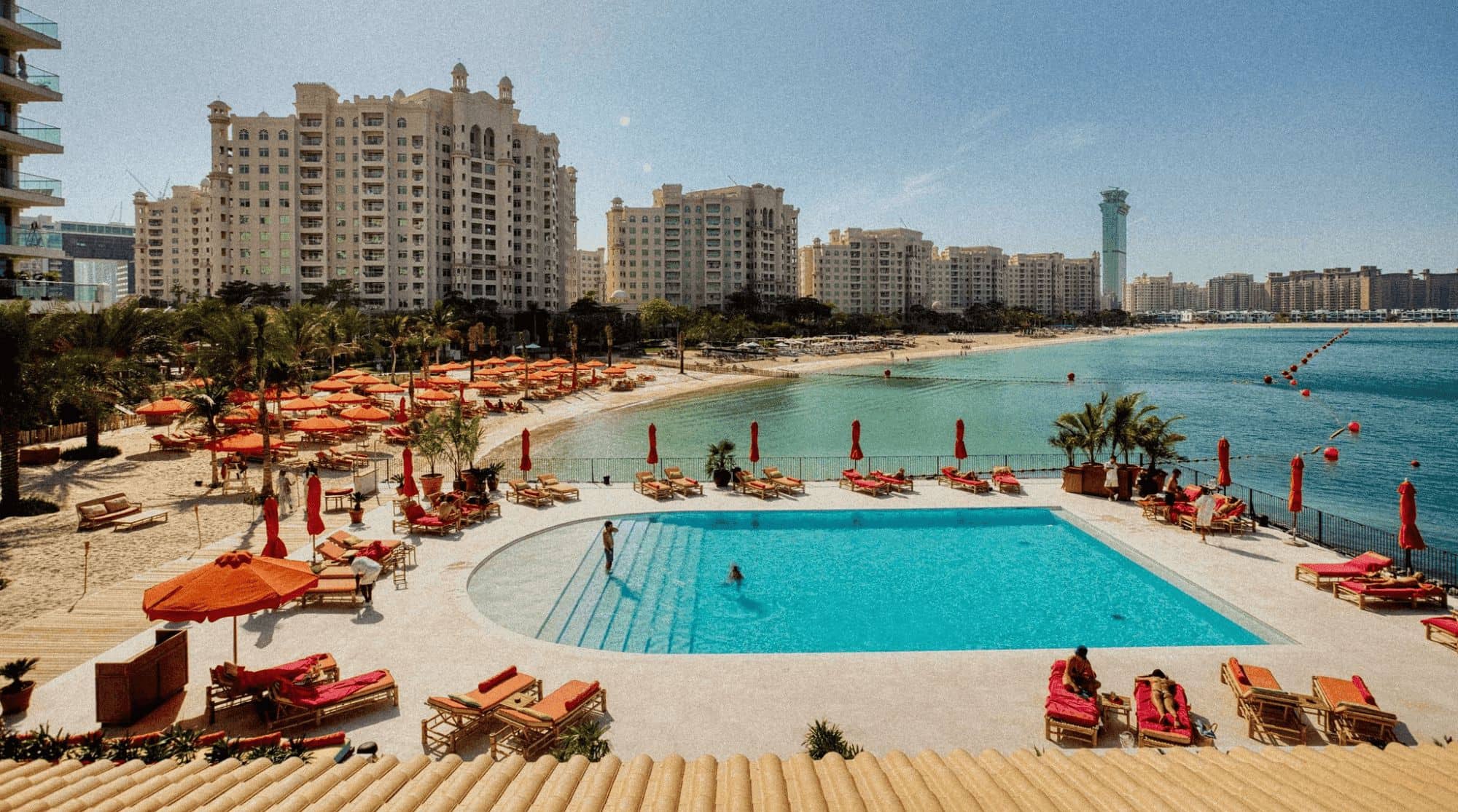 A luxury beach resort with red sun loungers and the city skyline in the background.