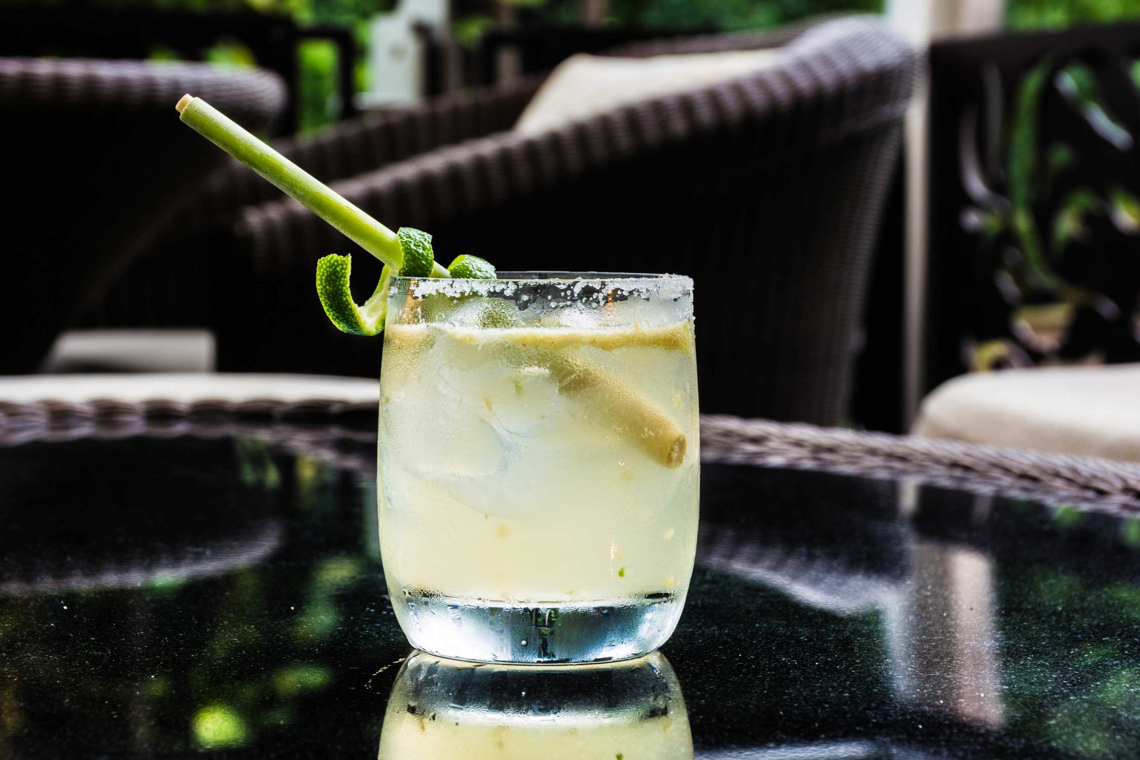 A lime and mint cocktail in a glass on a dark table outdoors with wicker chairs in the blurred background.