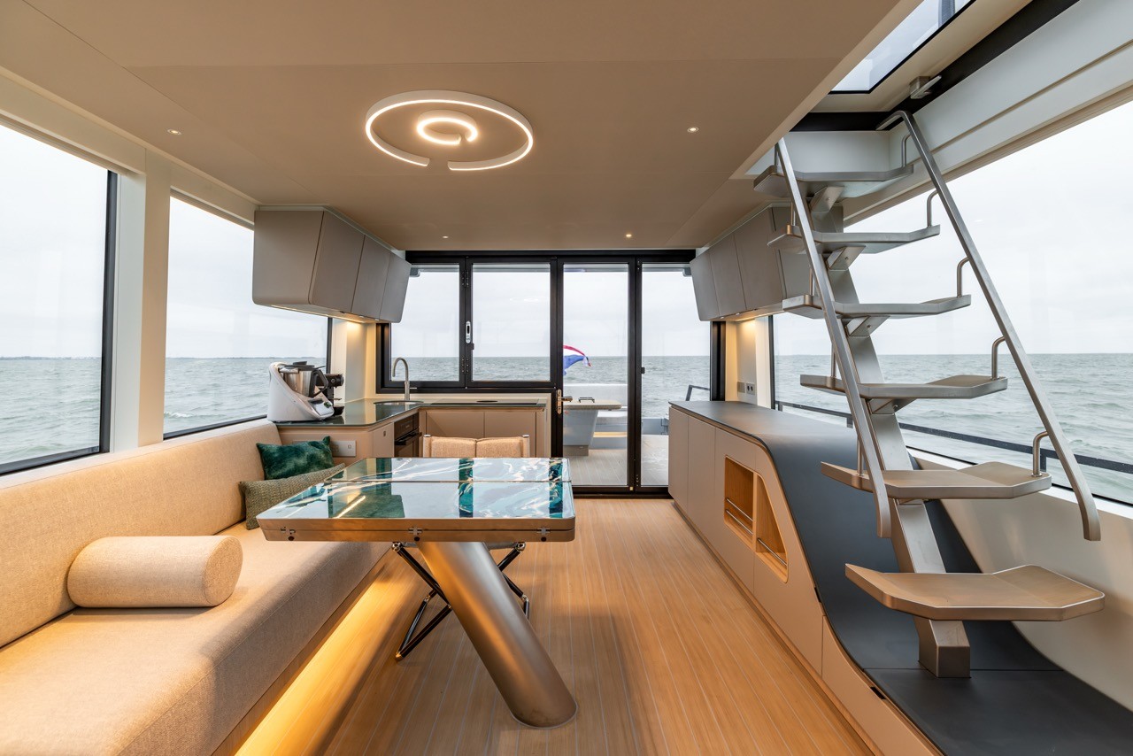 Motor yacht saloon interior featuring continuous EcoDeck composite flooring running from the interior saloon through to the aft cockpit via large sliding glass doors, showcasing EcoDeck's ability to create a seamless indoor-outdoor living flow in luxury yacht design