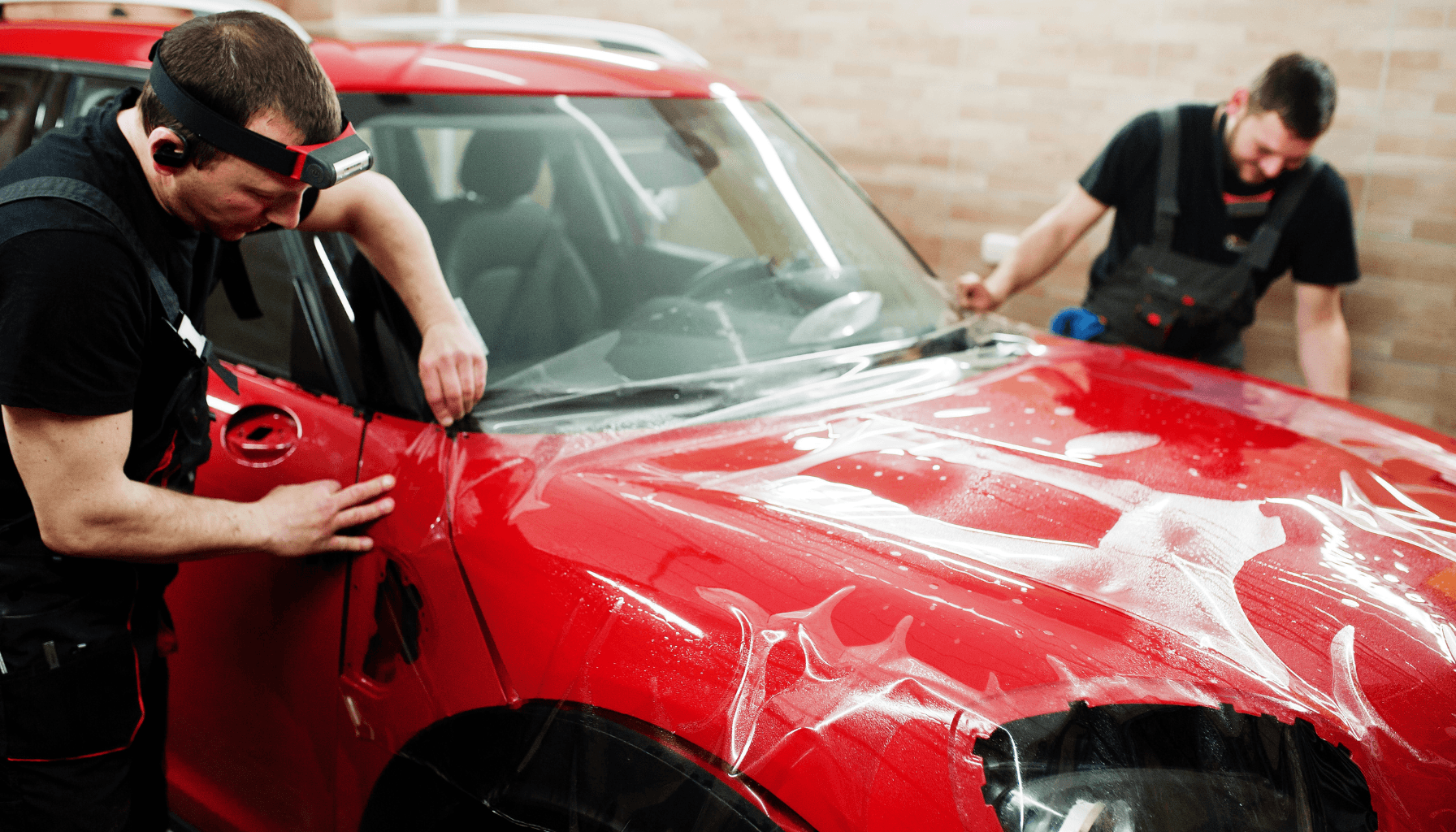 Zwei Personen bringen Lackschutzfolie auf die Motorhaube eines roten Autos auf.
