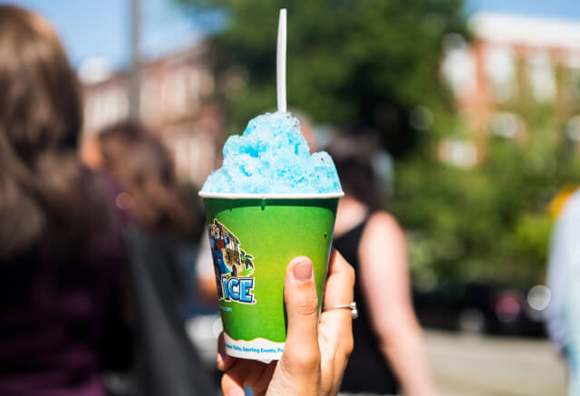 A hand holds a green cup filled with blue shaved ice and a white spoon