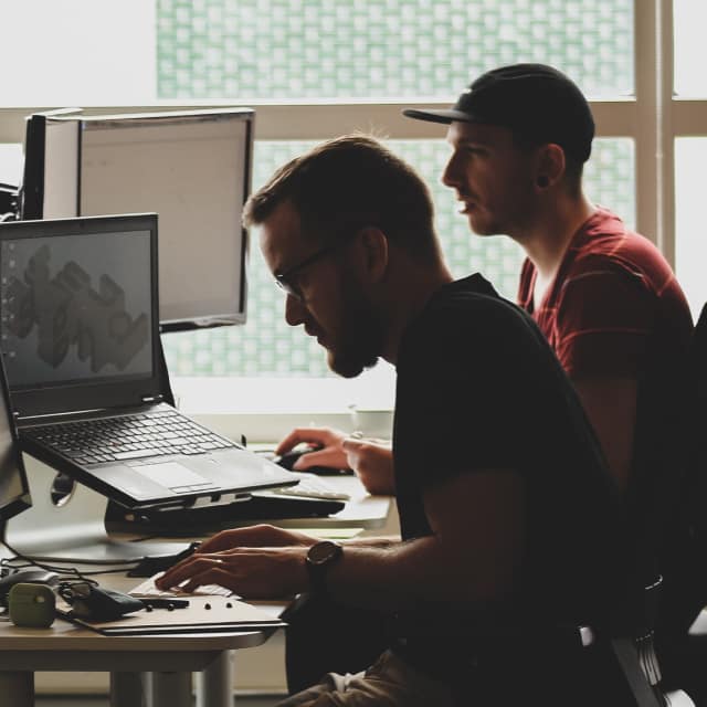 Two men in the office working on customer IT support on their computers.