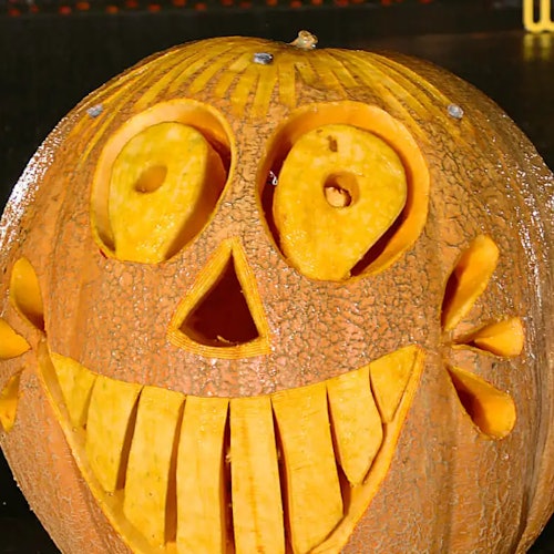 A carved pumpkin with a wide, toothy grin and large, circular eyes, resembling a joyful face.