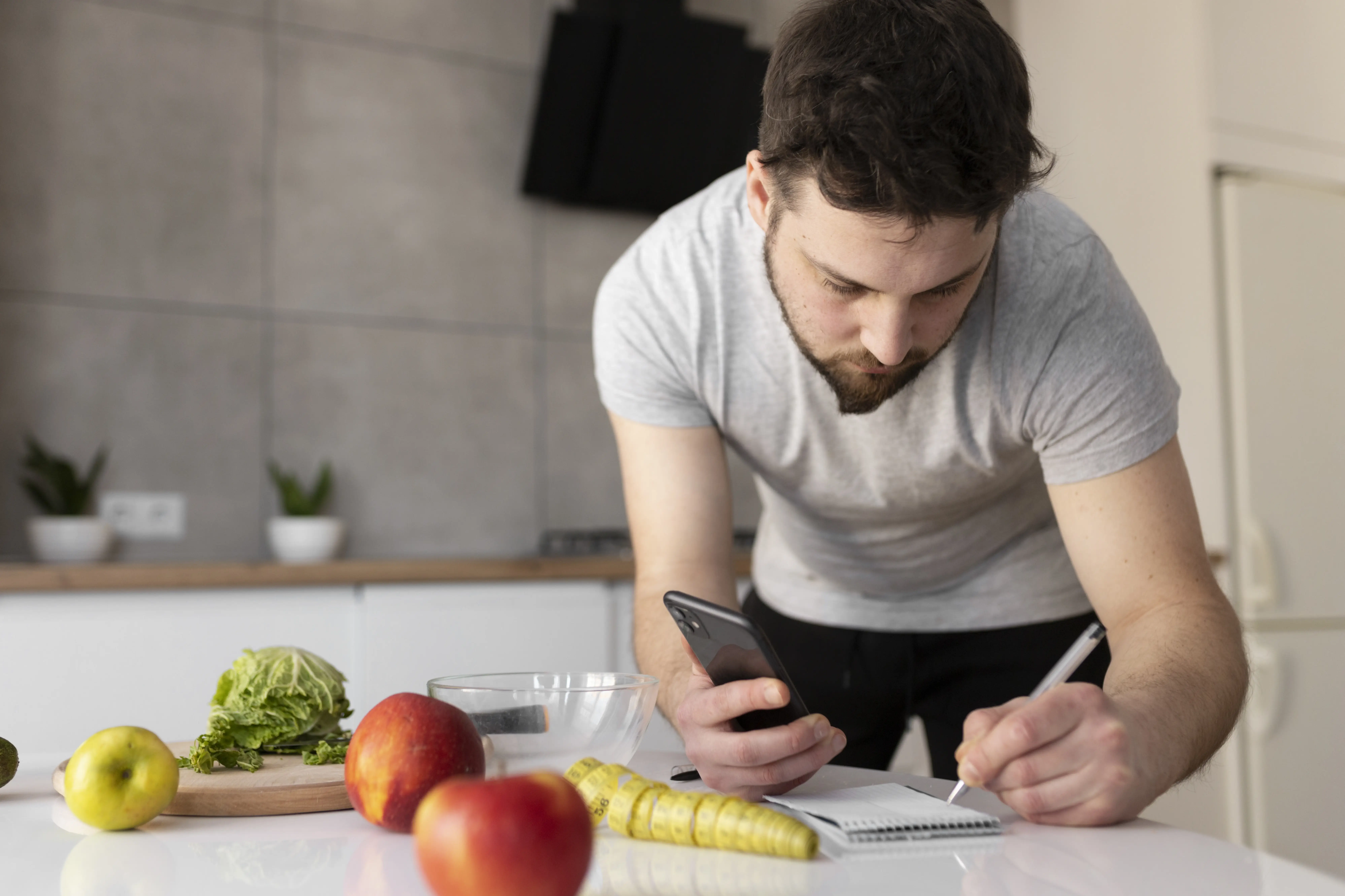 “Hombre revisando su plan de alimentación saludable con el celular, rodeado de frutas y verduras, retomando sus hábitos