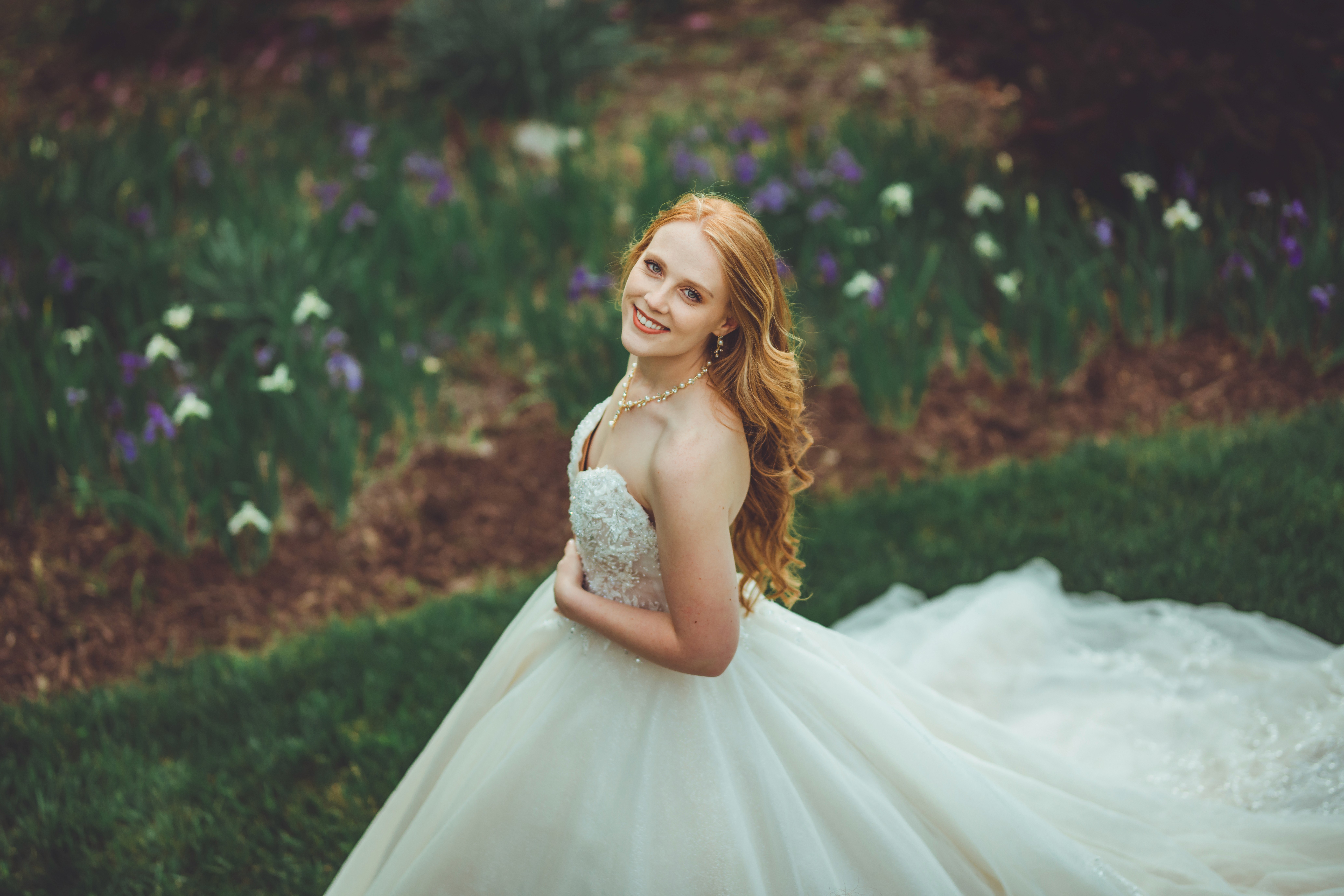 Couple embrace romantically outdoors. Woman in white dress, man in white shirt, standing on balcony with arms around each other.