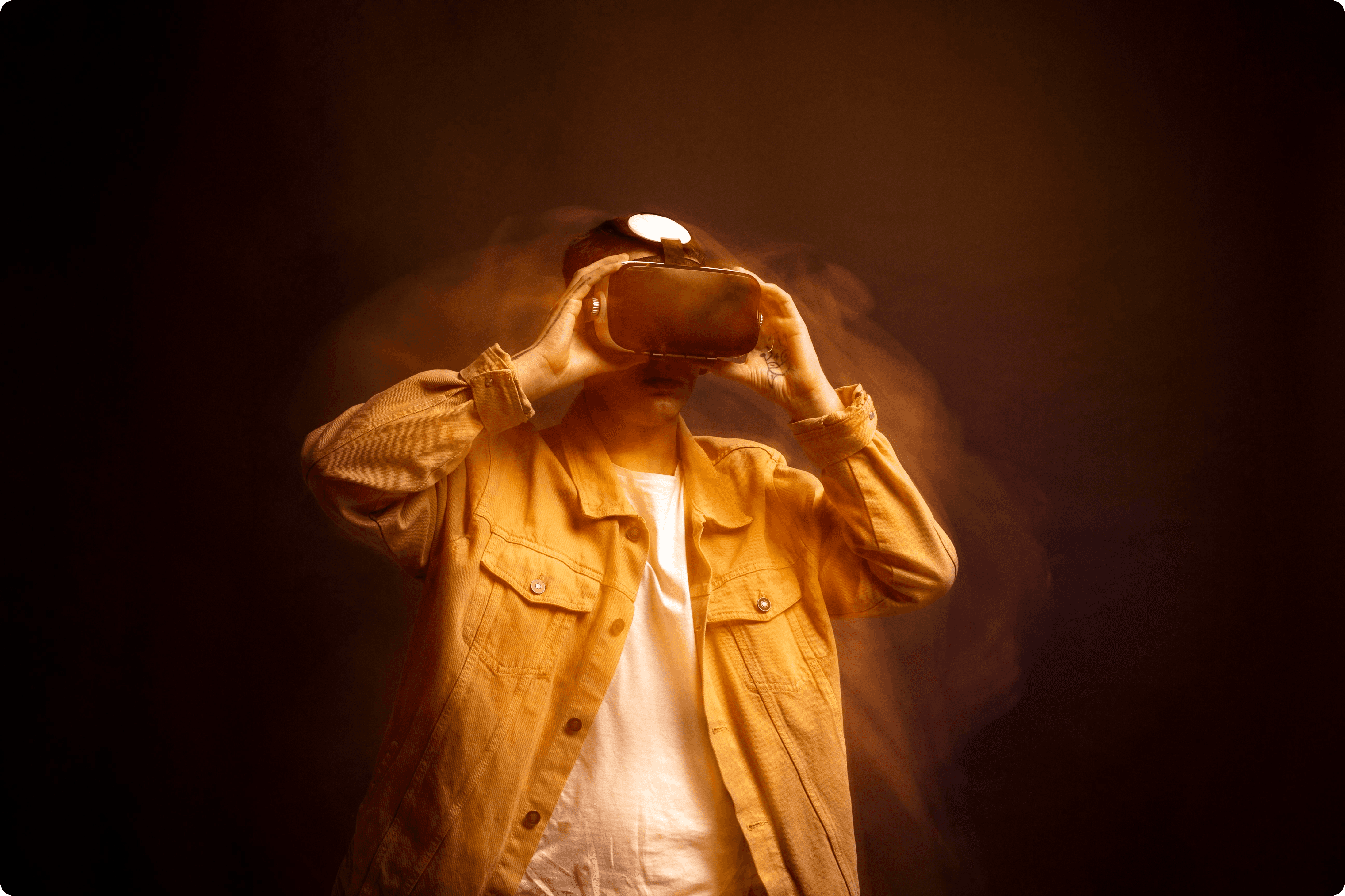 A cinematic portrait of a person adjusting a VR headset, featuring a long-exposure motion blur effect that creates a ghostly trail around their head and shoulders. The subject is wearing a mustard yellow denim jacket and a white t-shirt, set against a dark, smoky amber background with warm studio lighting.
