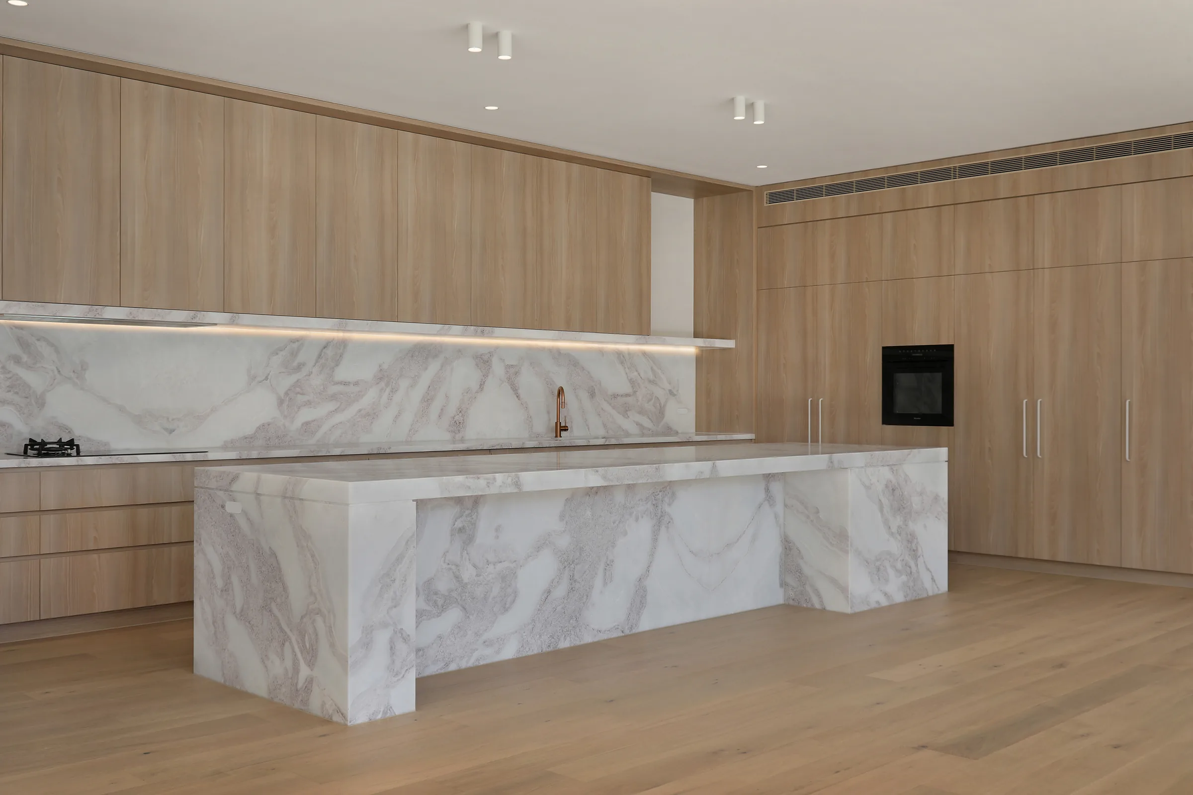 Kitchen with full-height oak cabinetry, a heavily veined white marble island and splashback, gas cooktop and copper tap