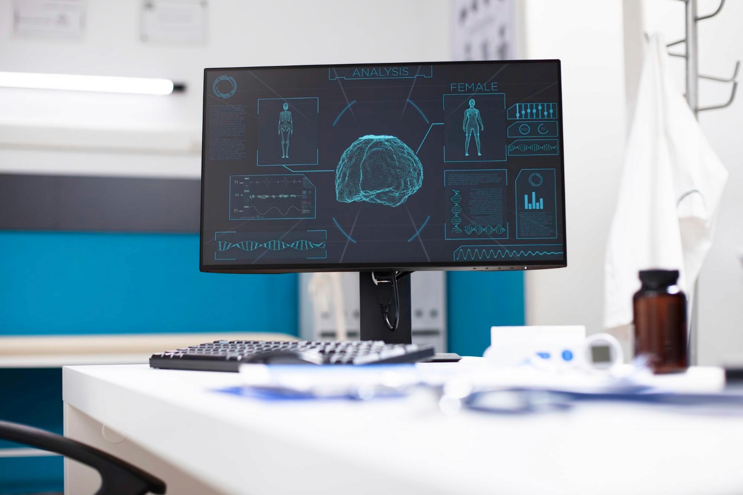 A computer monitor in a clinical setting shows a digital brain scan and medical data. A keyboard, mouse, and medicine bottle sit on the desk nearby.