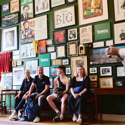 一組四個人坐在一張長椅上，房間裡有很多框架照片、海報和牆上的藝術品。