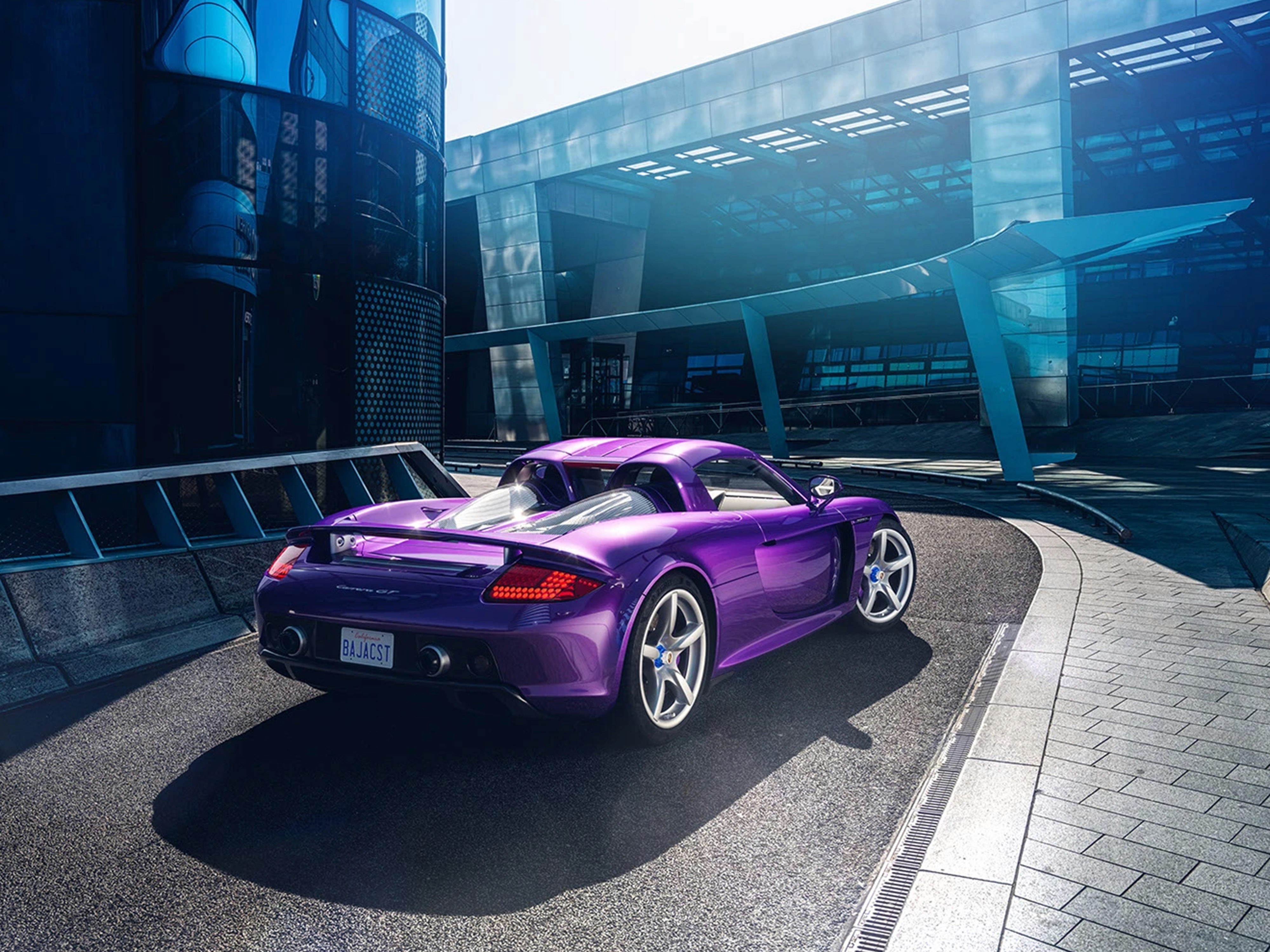 Porsche Carrera GT viola vista tre quarti posteriore in un contesto urbano moderno con edifici in vetro.