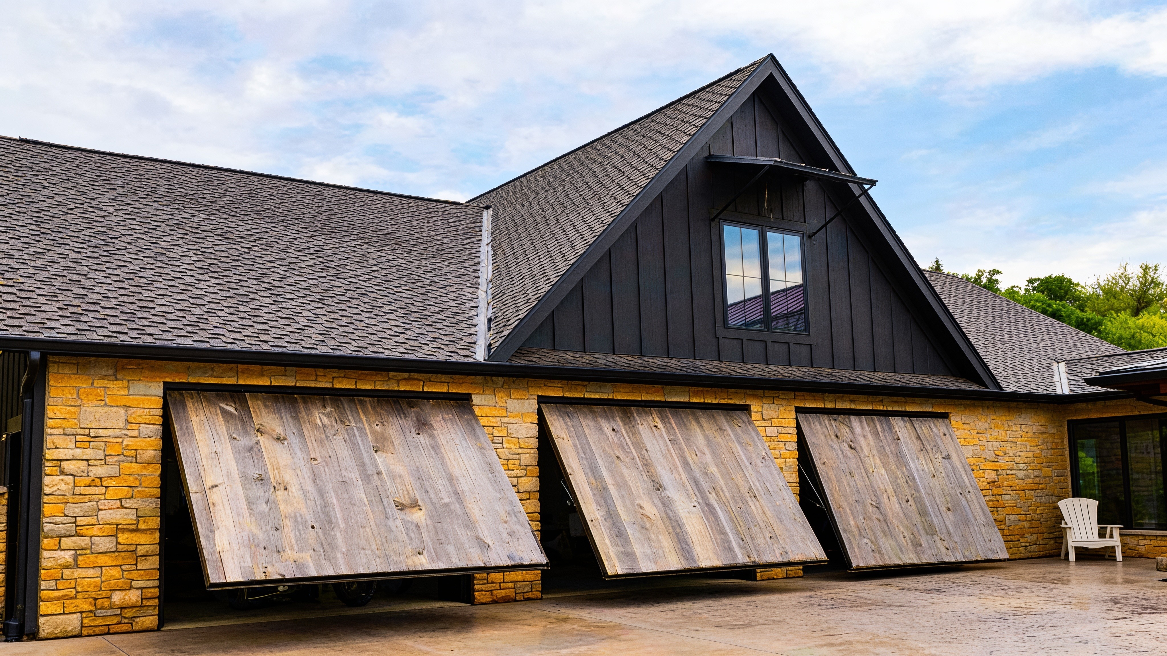 Three concealed cylinder wood garage doors on a modern black barn-style home